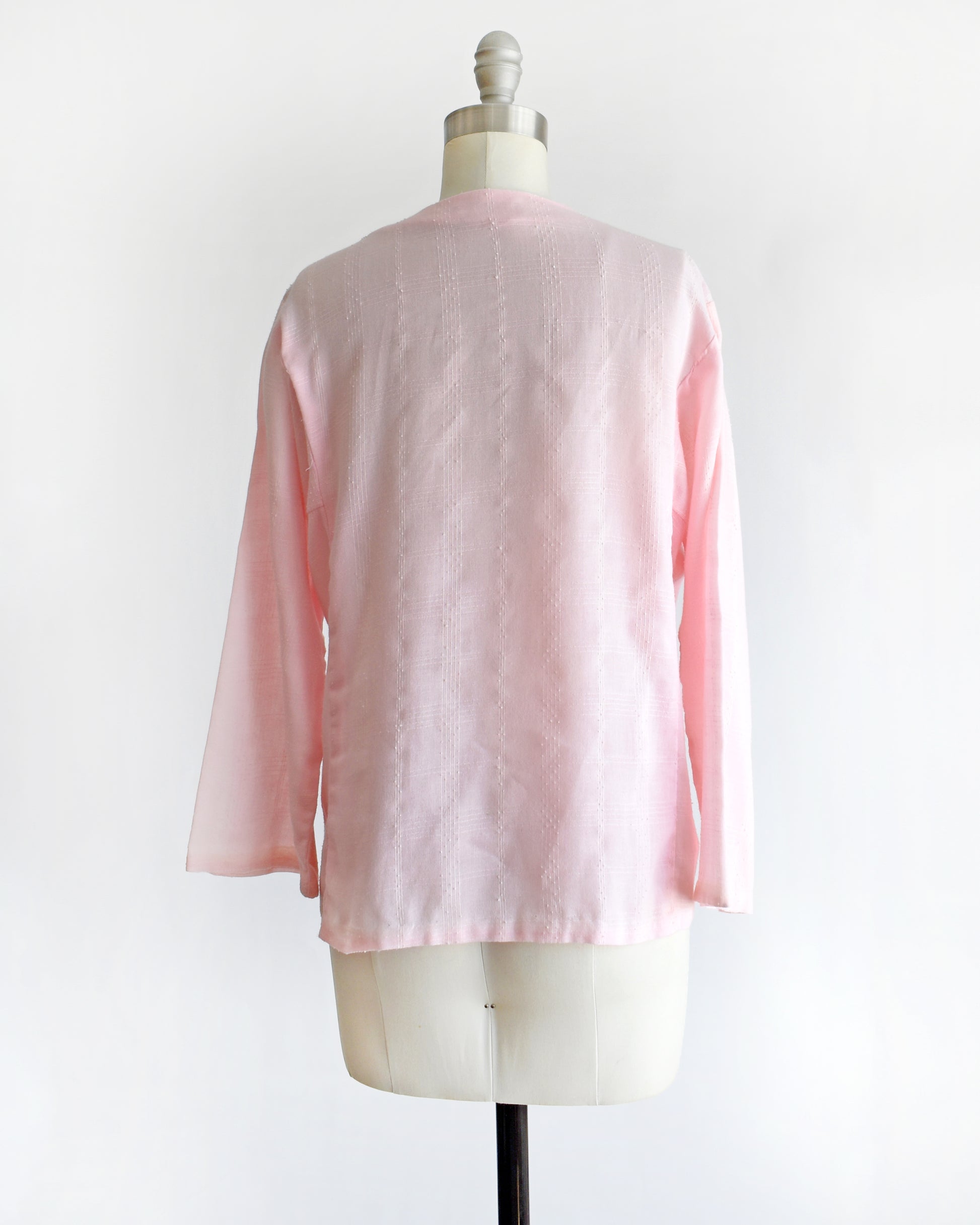 back view of a vintage pink blouse with floral embroidery on a mannequin against a white background