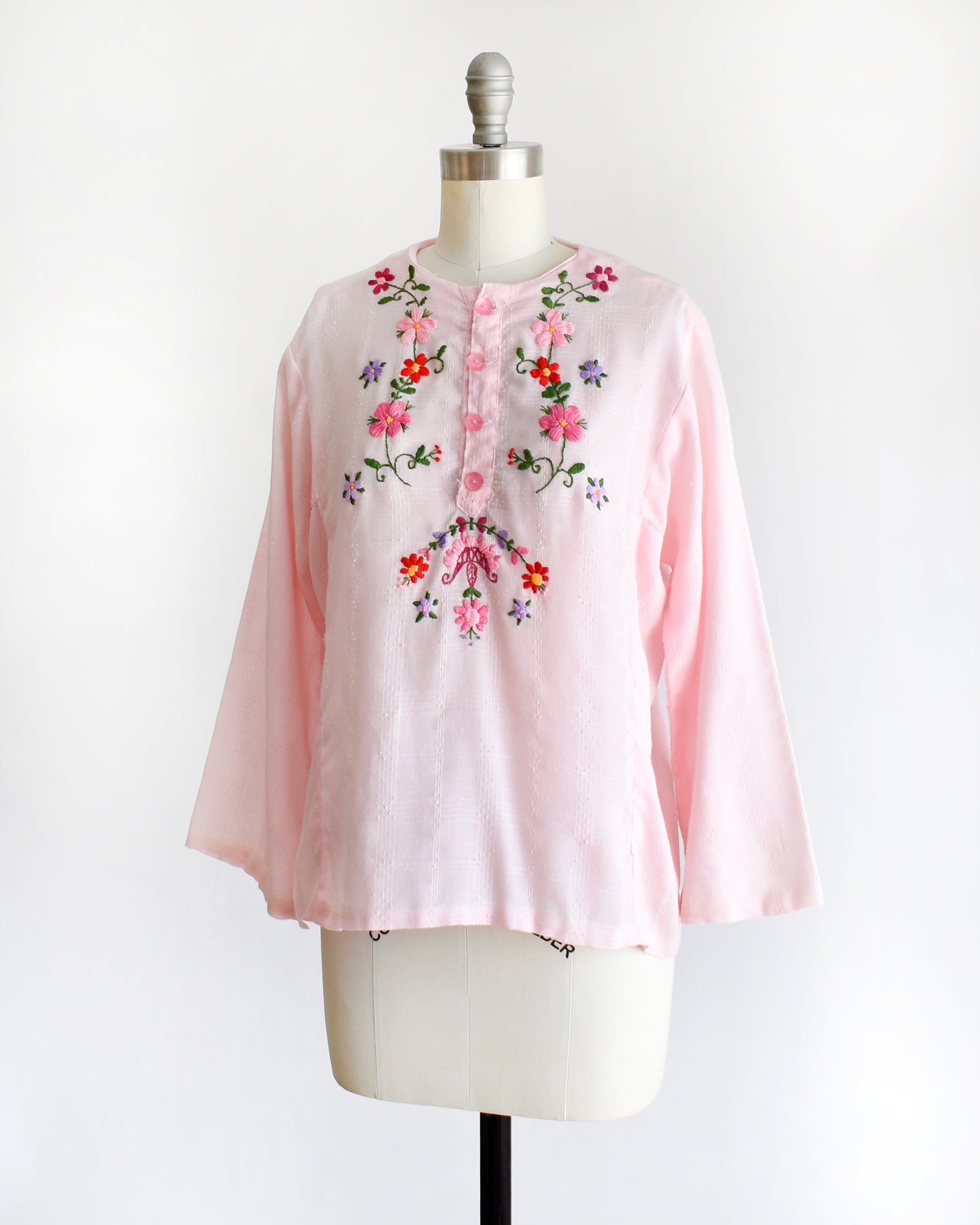 side front view of a vintage pink blouse with floral embroidery on a mannequin against a white background