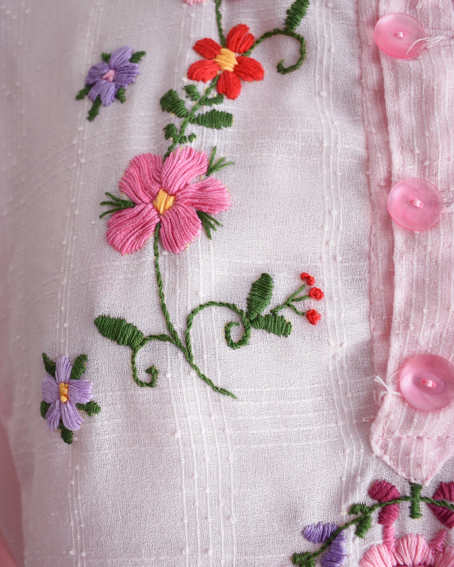 Close-up of embroidered flowers on a fabric with pink buttons.