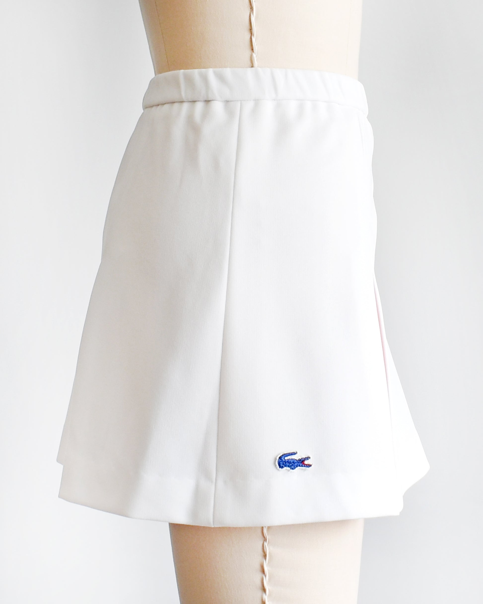 side view of a vintage 1970s Lacoste Haymaker skirt that has a blue Lacoste crocodile on the side on a mannequin against a white background