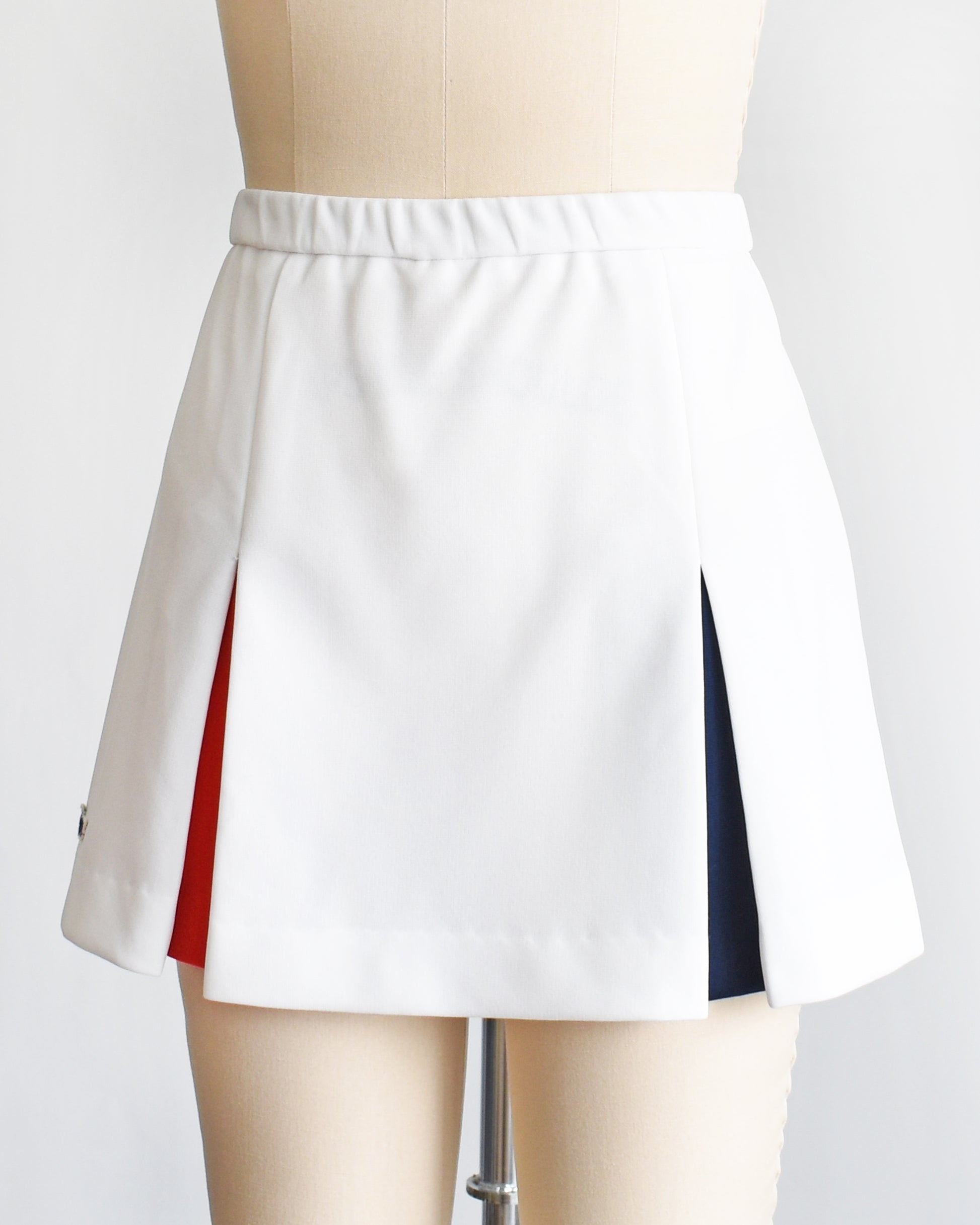side front view of a vintage 1970s Lacoste Haymaker skirt with red and blue accented pleats on a mannequin against a white background
