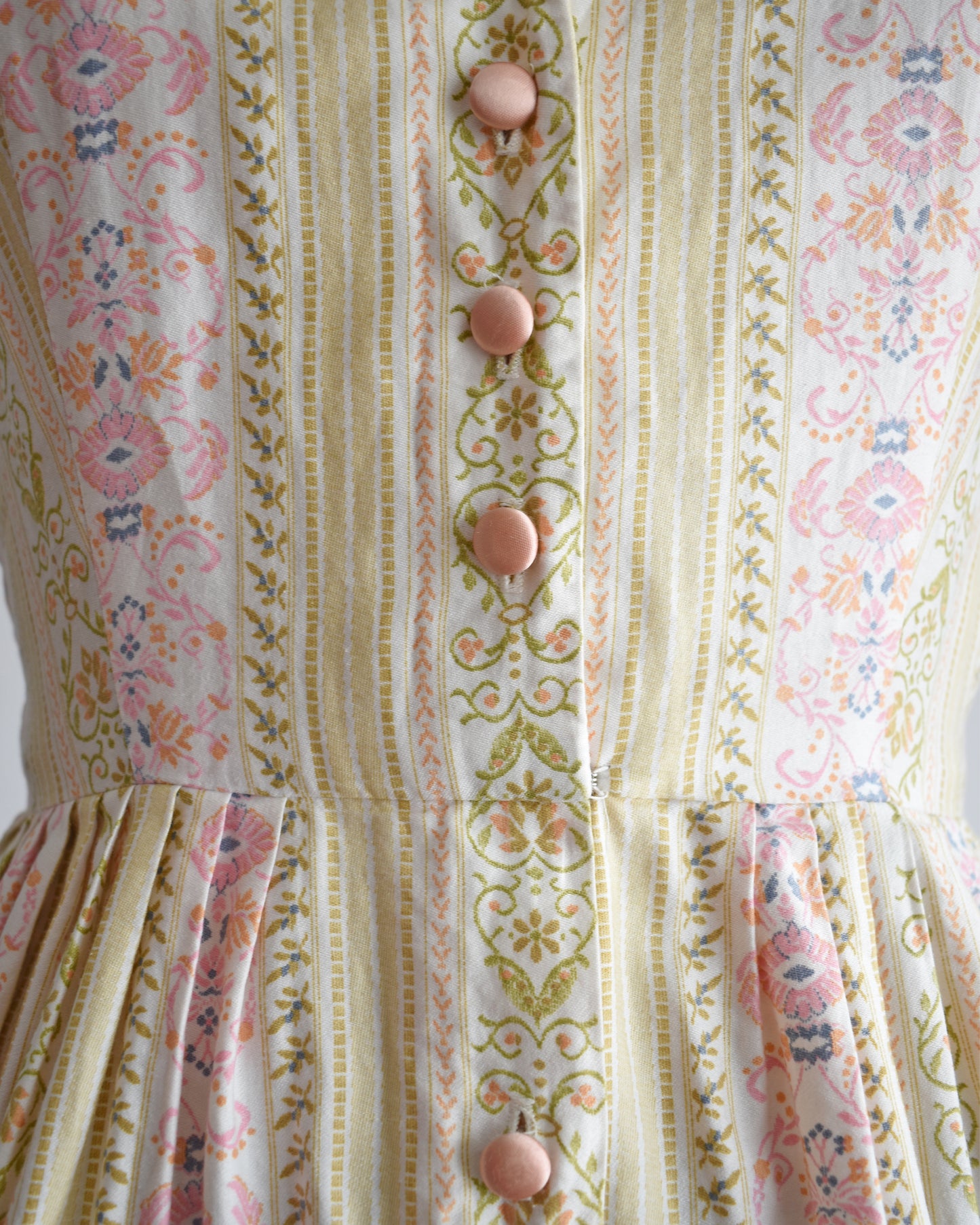 Close-up of a patterned dress with floral and striped design and pink buttons.