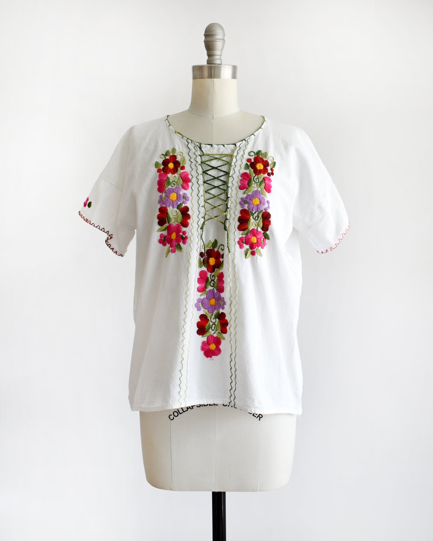 a vintage 1970s white blouse with colorful floral embroidery on a mannequin against a white background