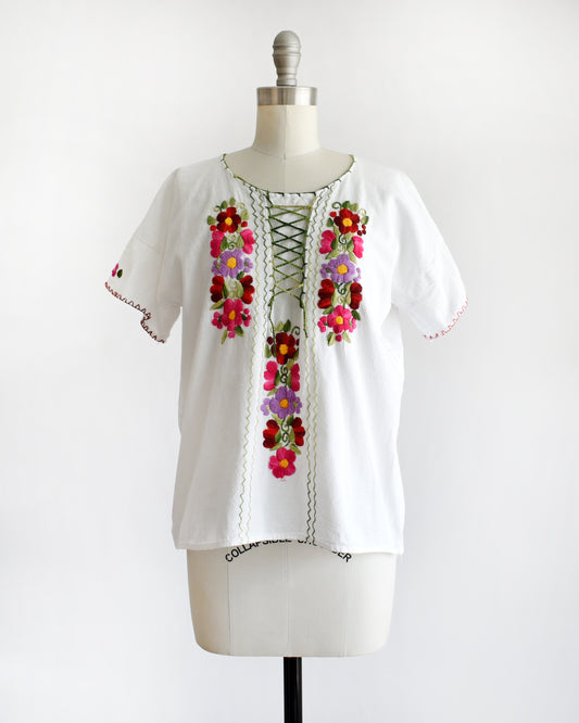 a vintage 1970s white blouse with colorful floral embroidery on a mannequin against a white background