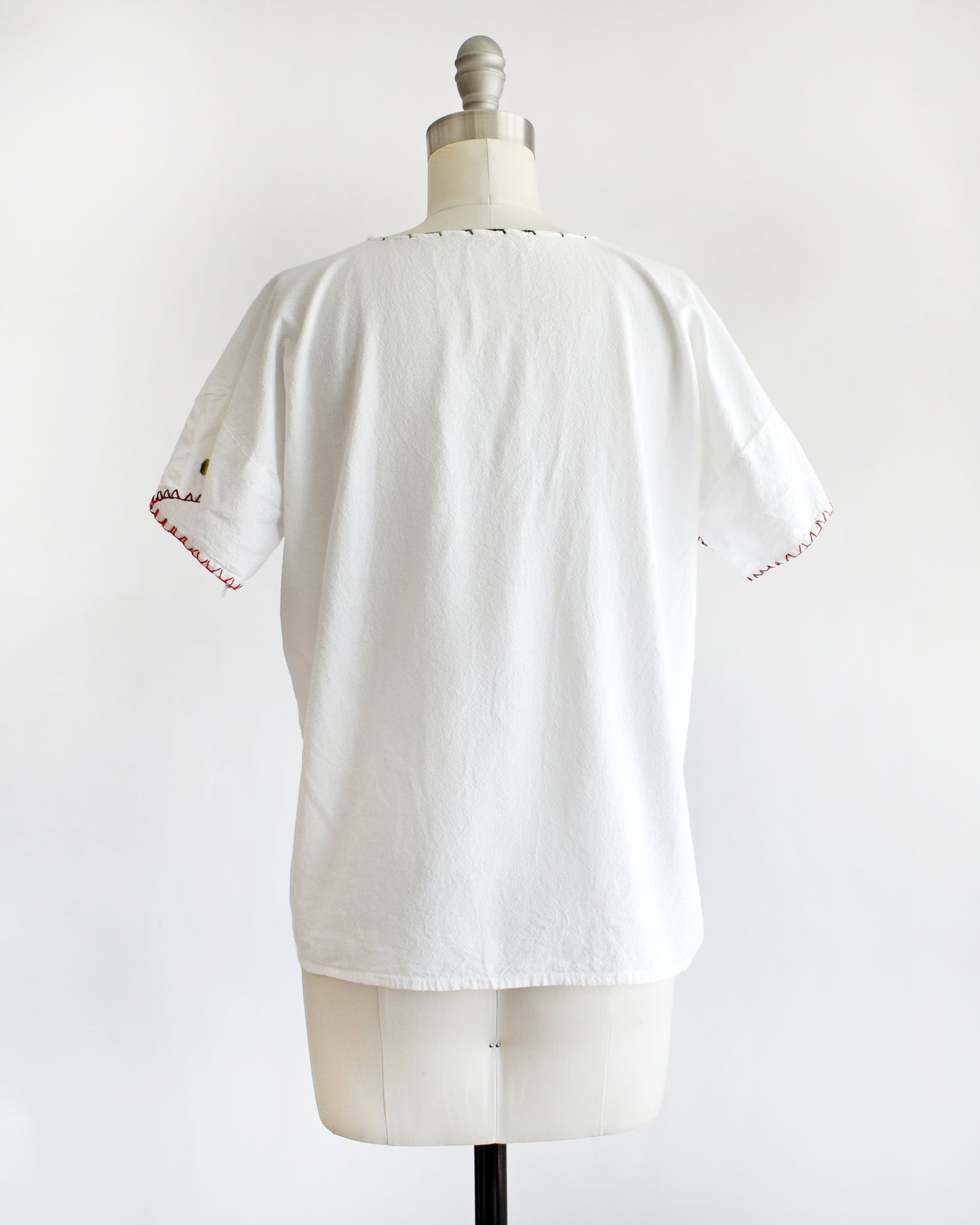 back view of a vintage 1970s white blouse with colorful floral embroidery on a mannequin against a white background