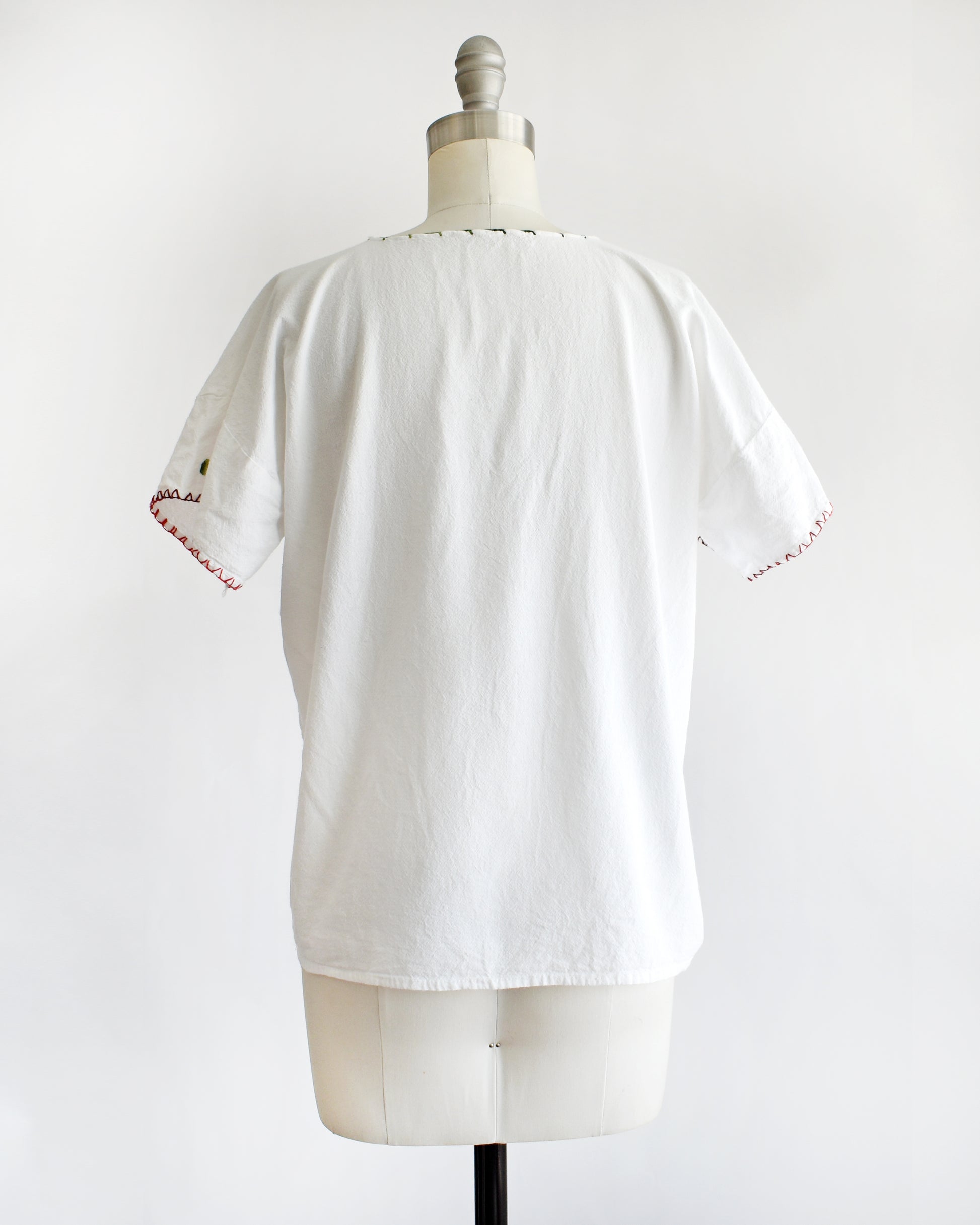 back view of a vintage 1970s white blouse with colorful floral embroidery on a mannequin against a white background
