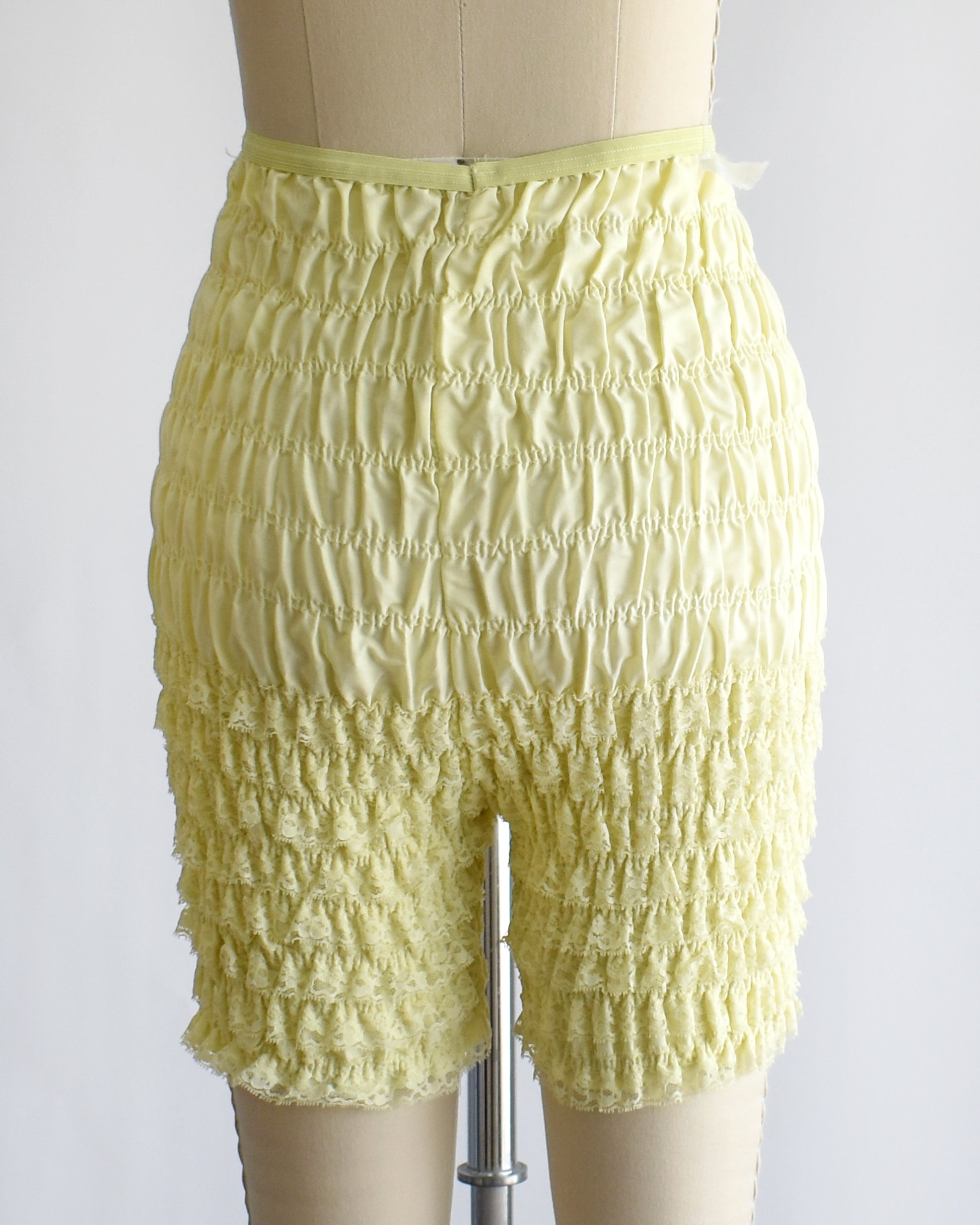 back view of vintage yellow ruffled shorts on a mannequin against a white background