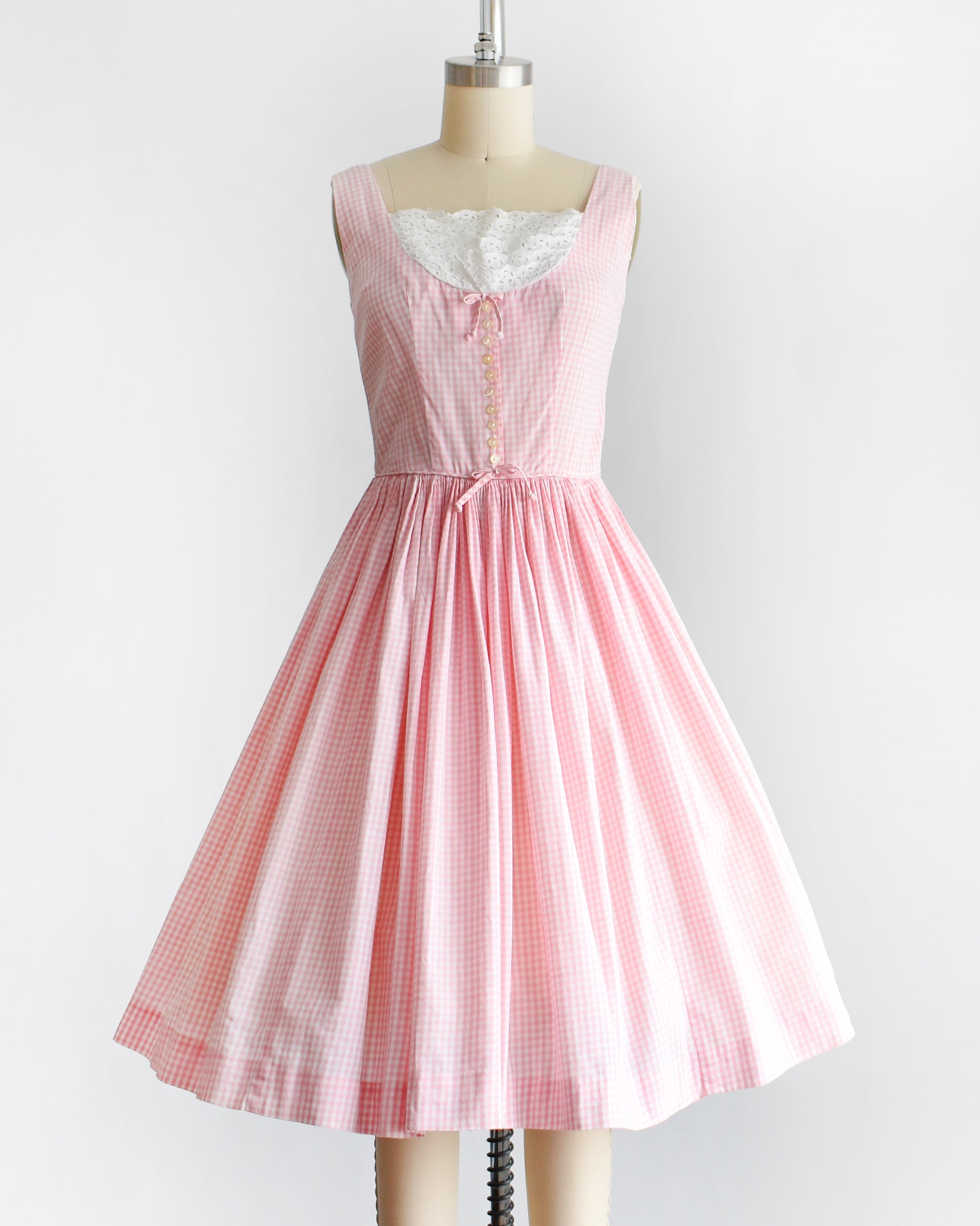 a vintage 1950s pink and white gingham dress on a mannequin against a white background