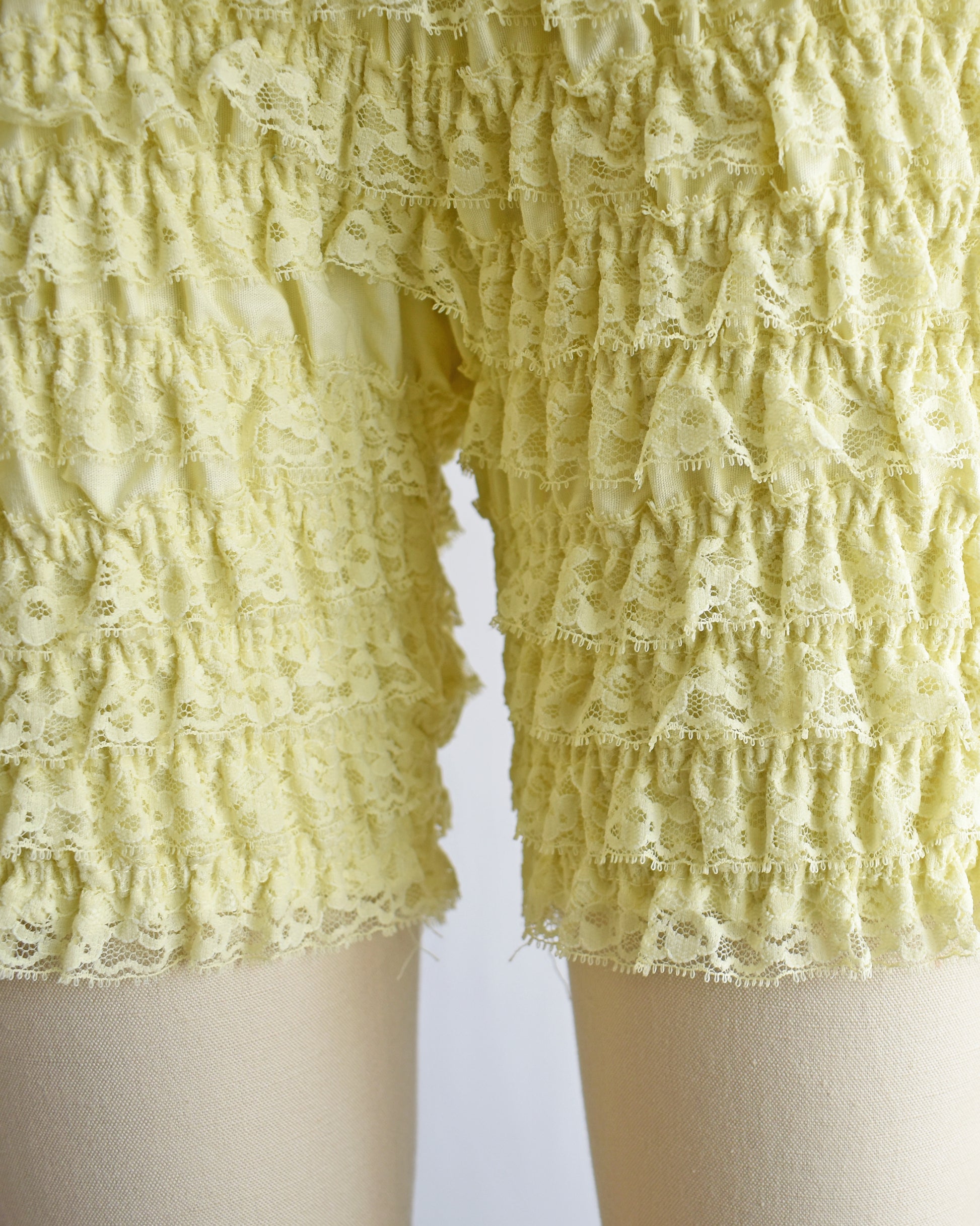 close up of the legs on a pair of vintage yellow ruffled shorts on a mannequin against a white background