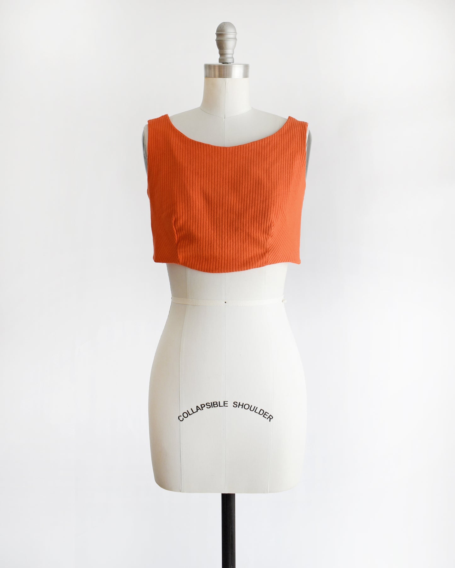 a vintage 1970s orange sleeveless crop top on a mannequin with 'Collapsible Shoulder' label against a white background