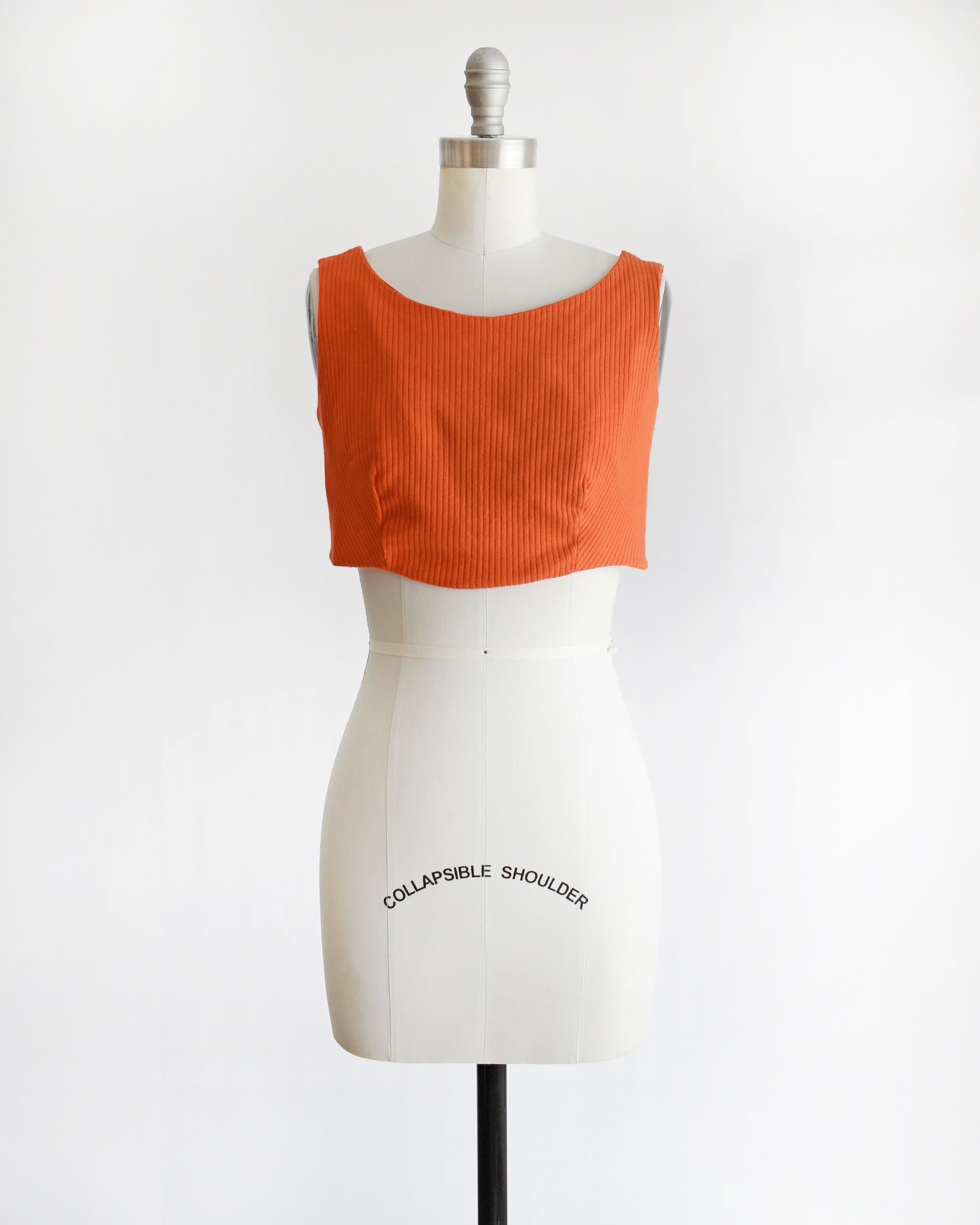 a vintage 1970s orange sleeveless crop top on a mannequin with 'Collapsible Shoulder' label against a white background