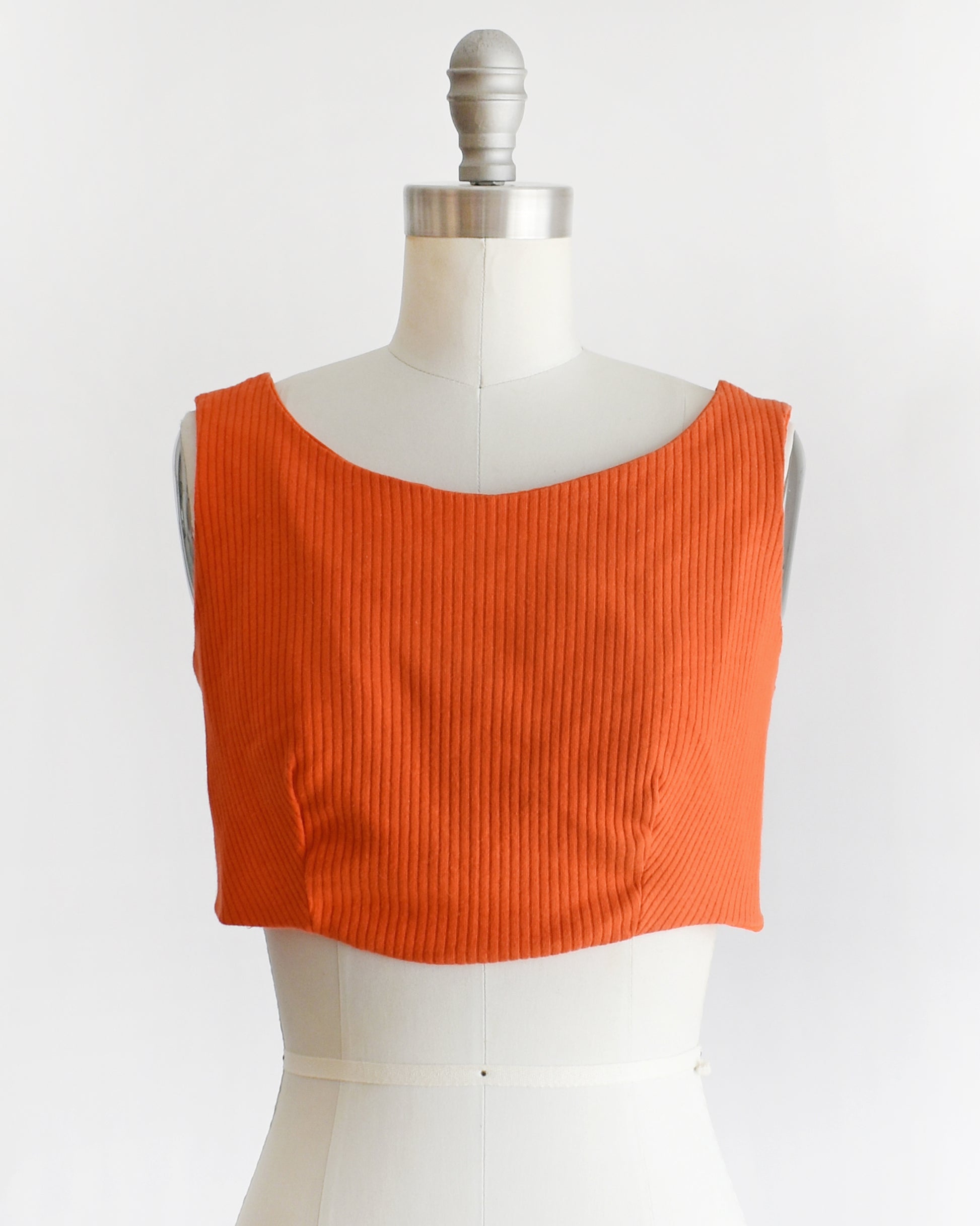 a vintage 1970s orange sleeveless crop top on a mannequin with 'Collapsible Shoulder' label against a white background
