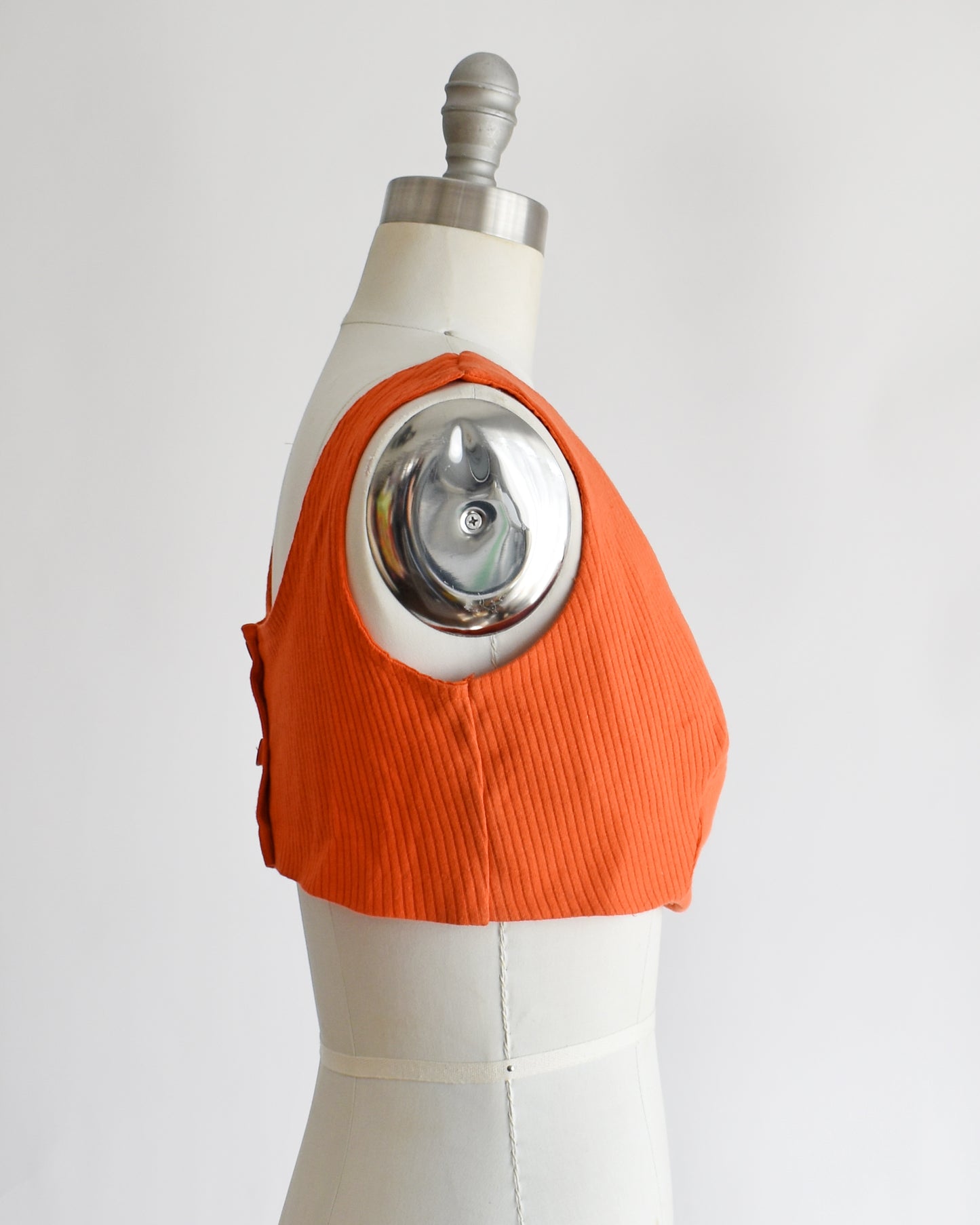 side view of a vintage 1970s orange sleeveless crop top on a mannequin with 'Collapsible Shoulder' label against a white background