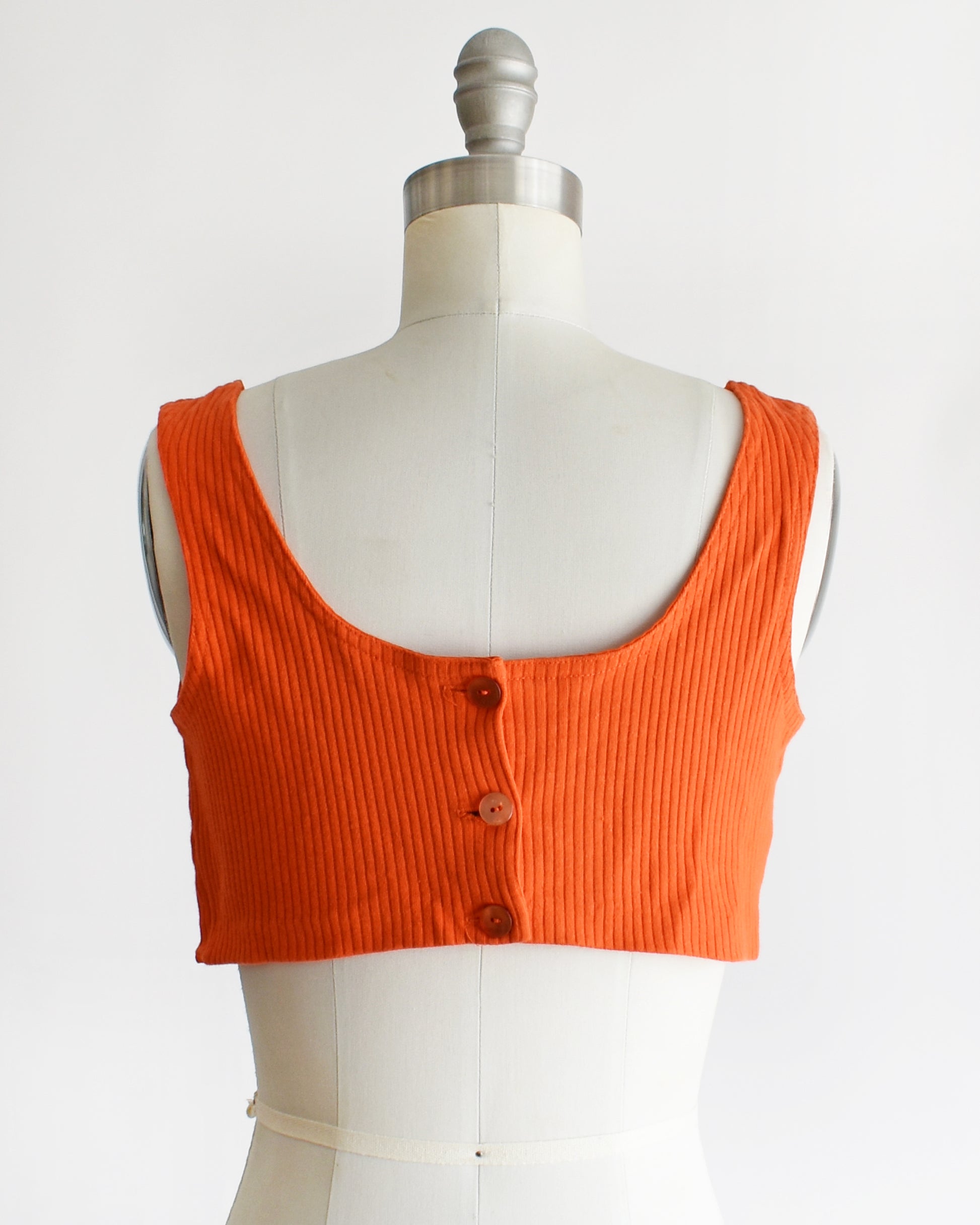 back view of a vintage 1970s orange sleeveless crop top on a mannequin with 'Collapsible Shoulder' label against a white background