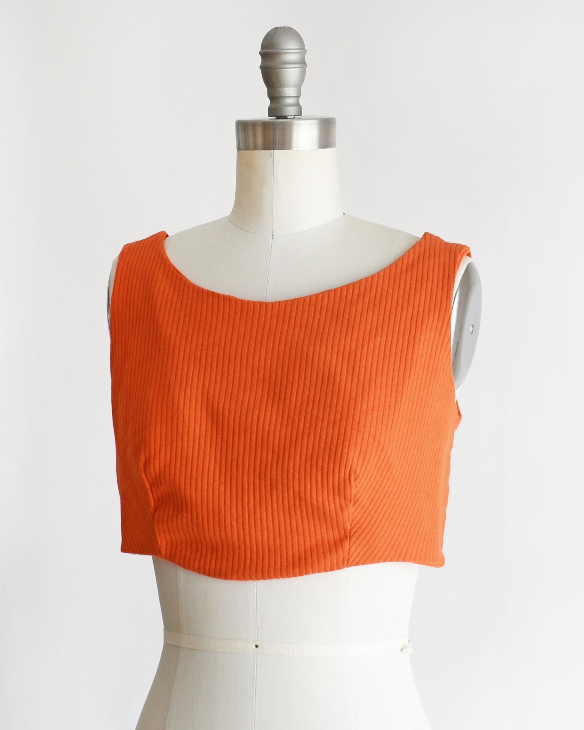 side front view of a vintage 1970s orange sleeveless crop top on a mannequin with 'Collapsible Shoulder' label against a white background