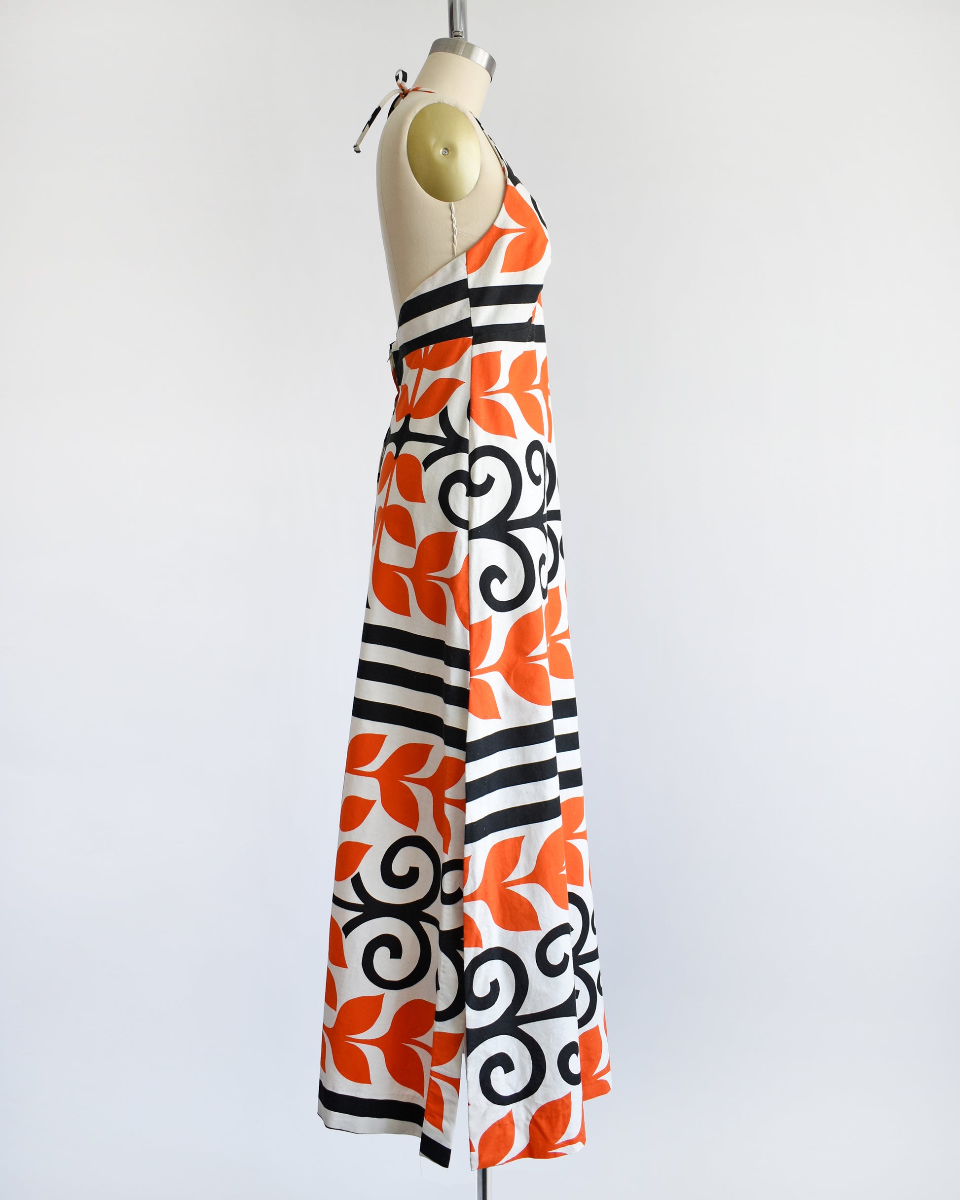 side view of a vintage 1970s Baba Kea Hawaiian white halter dress that has a bold orange and black print