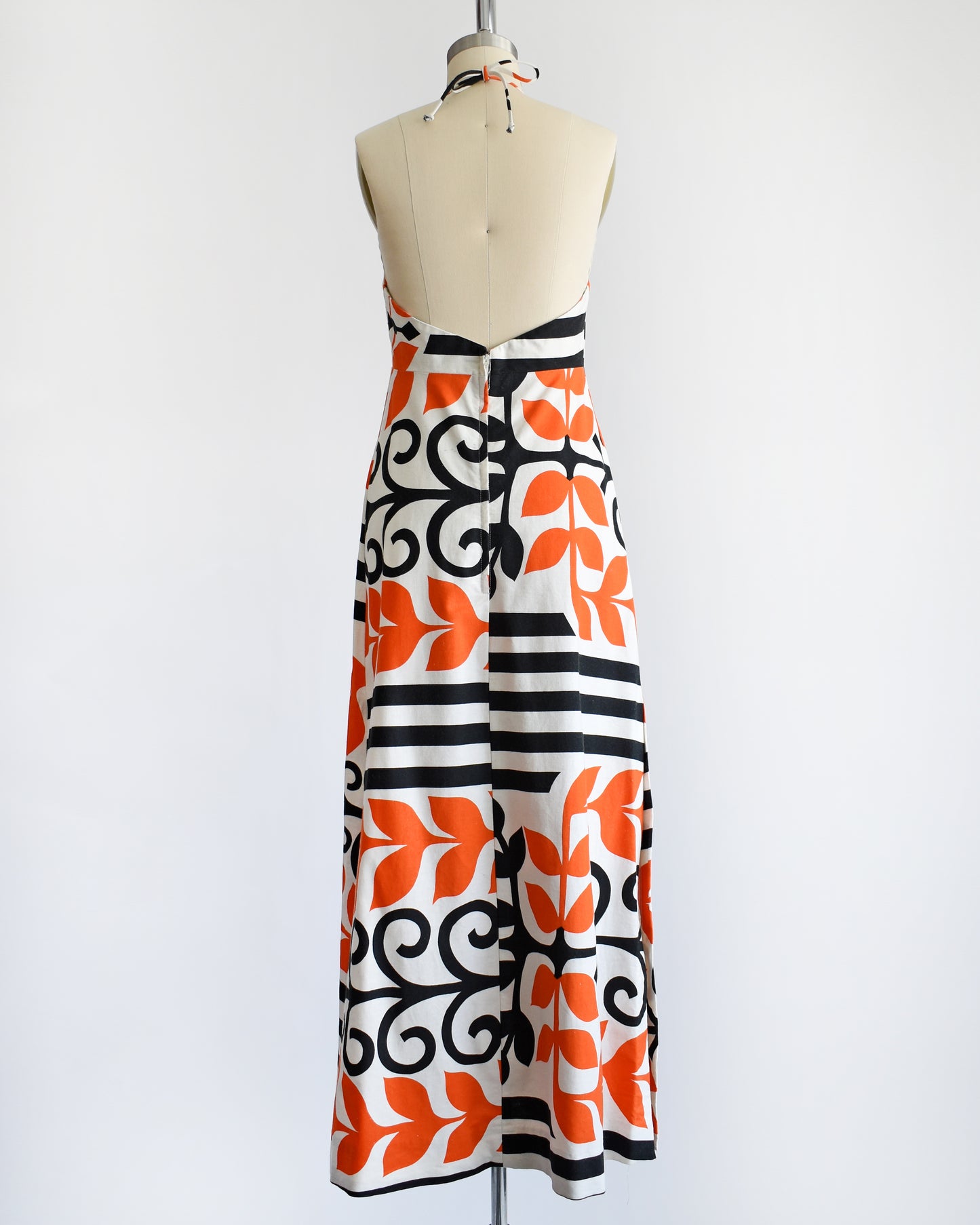 back view of a vintage 1970s Baba Kea Hawaiian white halter dress that has a bold orange and black print