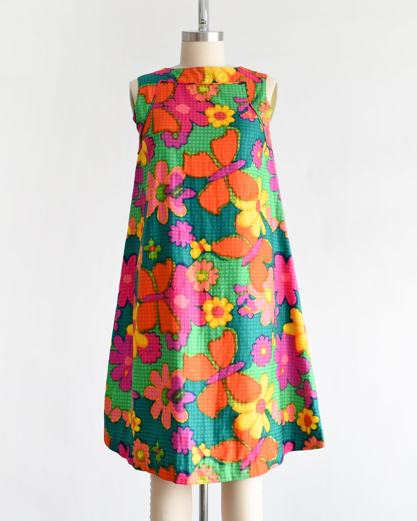 a vintage 1960s colorful floral dress on a mannequin against a white background