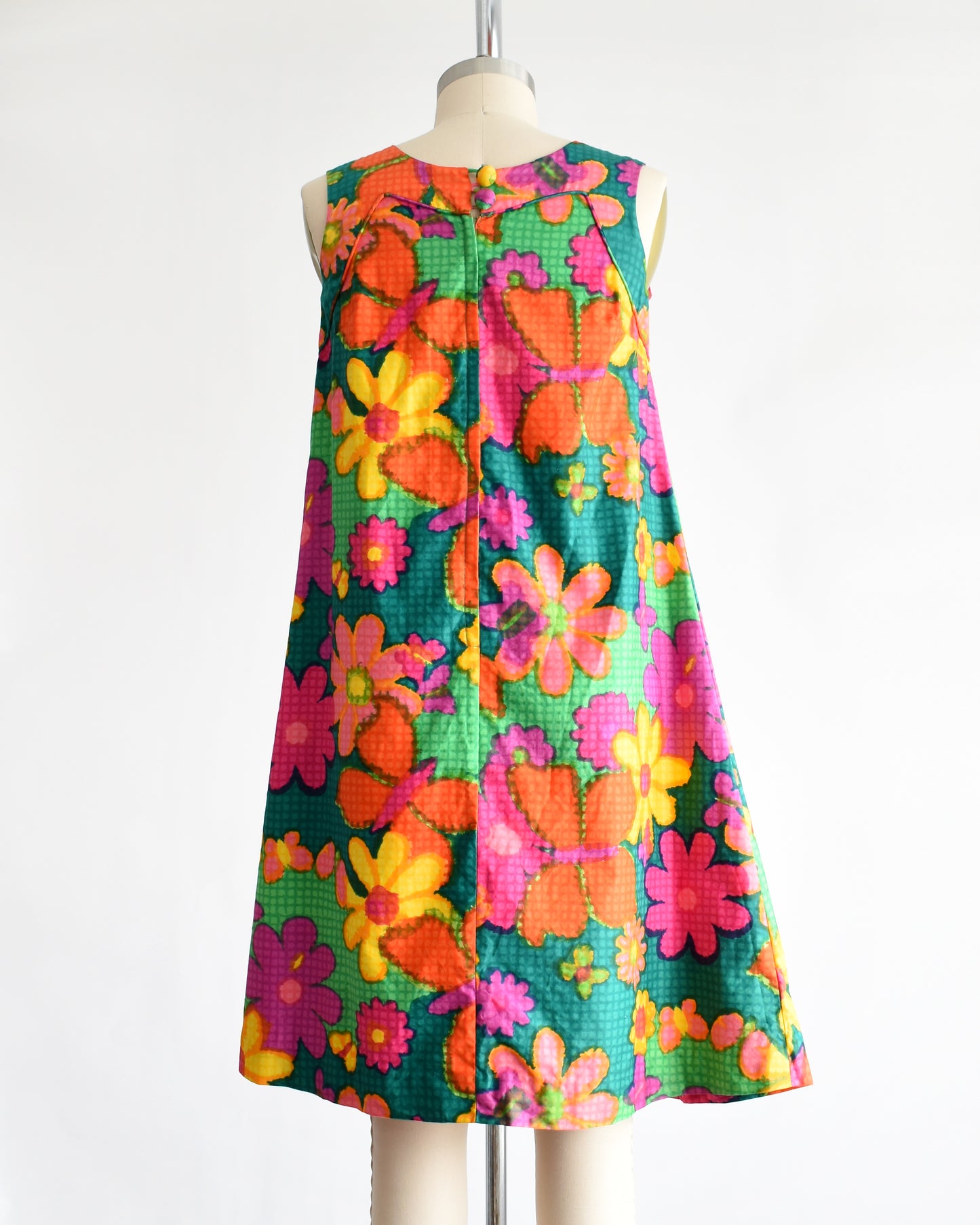 back view of a vintage 1960s colorful floral dress on a mannequin against a white background