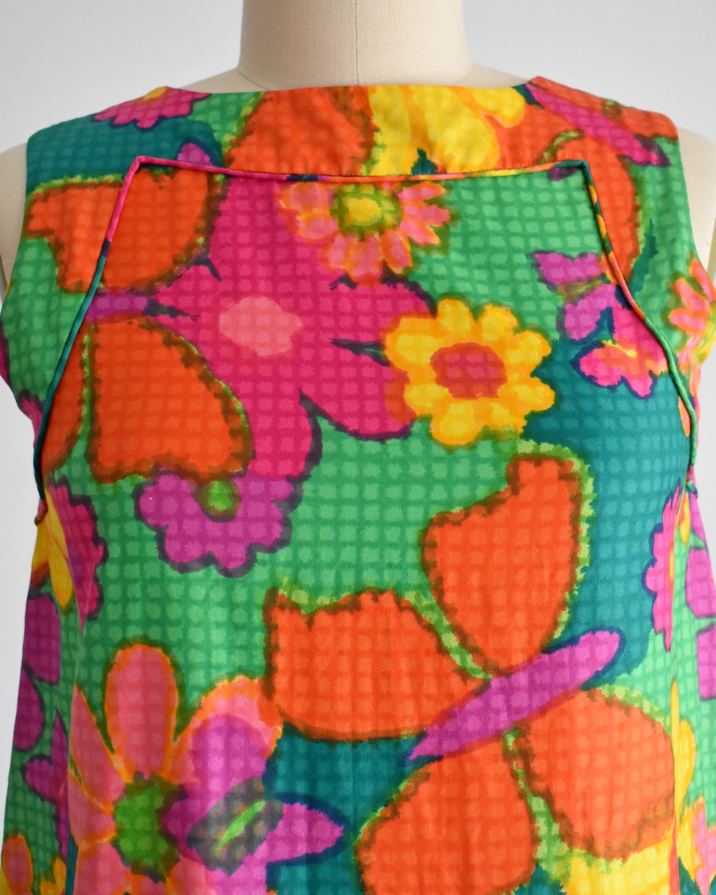 close up of the bodice of a vintage 1960s colorful floral dress on a mannequin against a white background