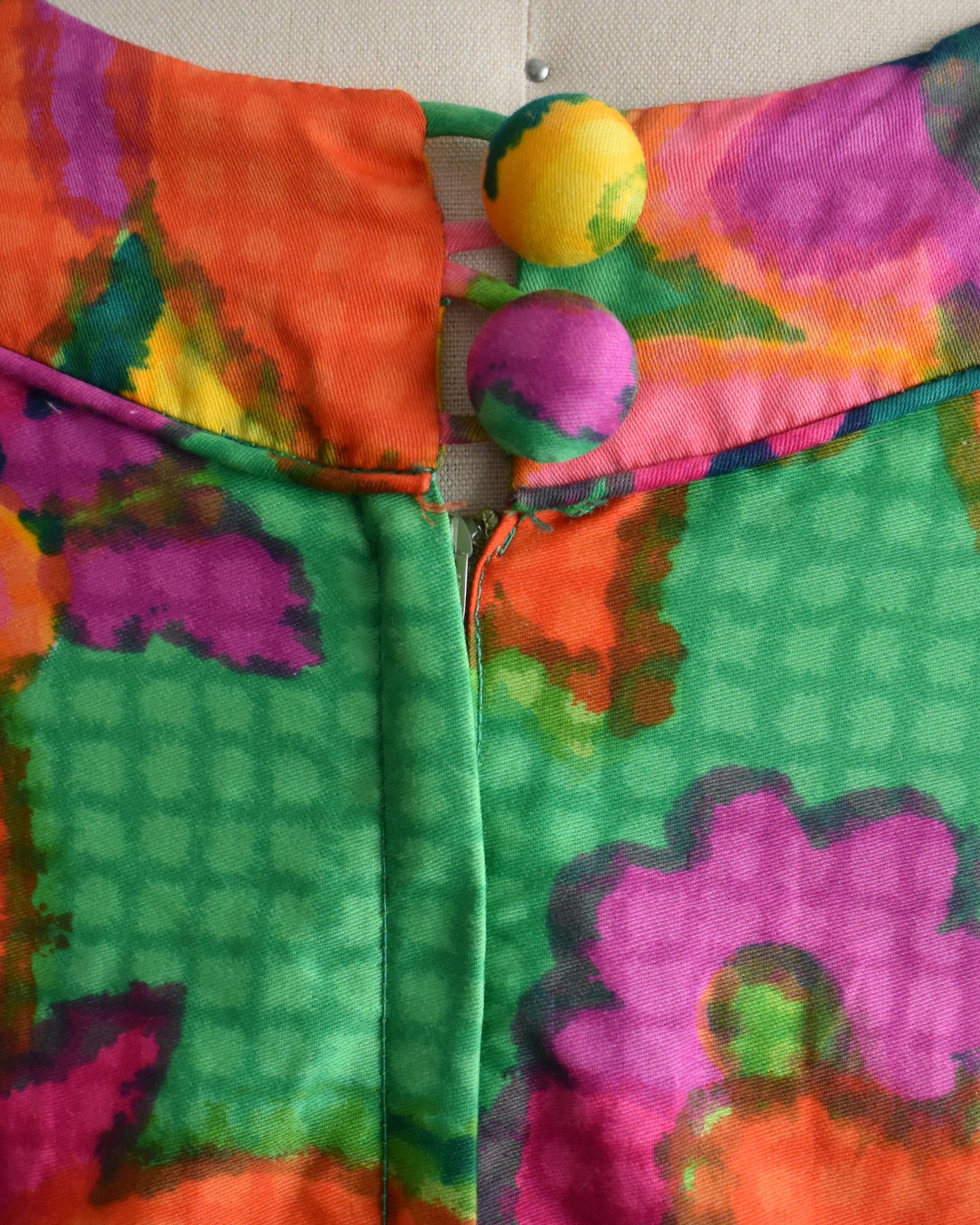 close up of the back buttons on a vintage 1960s colorful floral dress on a mannequin against a white background