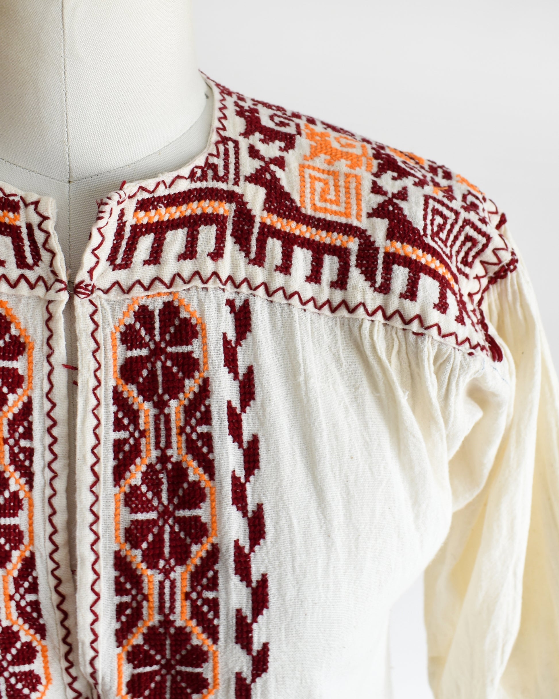 Close up of the burgundy and orange embroidered floral and what looks like llamas motif across the shoulders and down the front. The top is on a dress form.