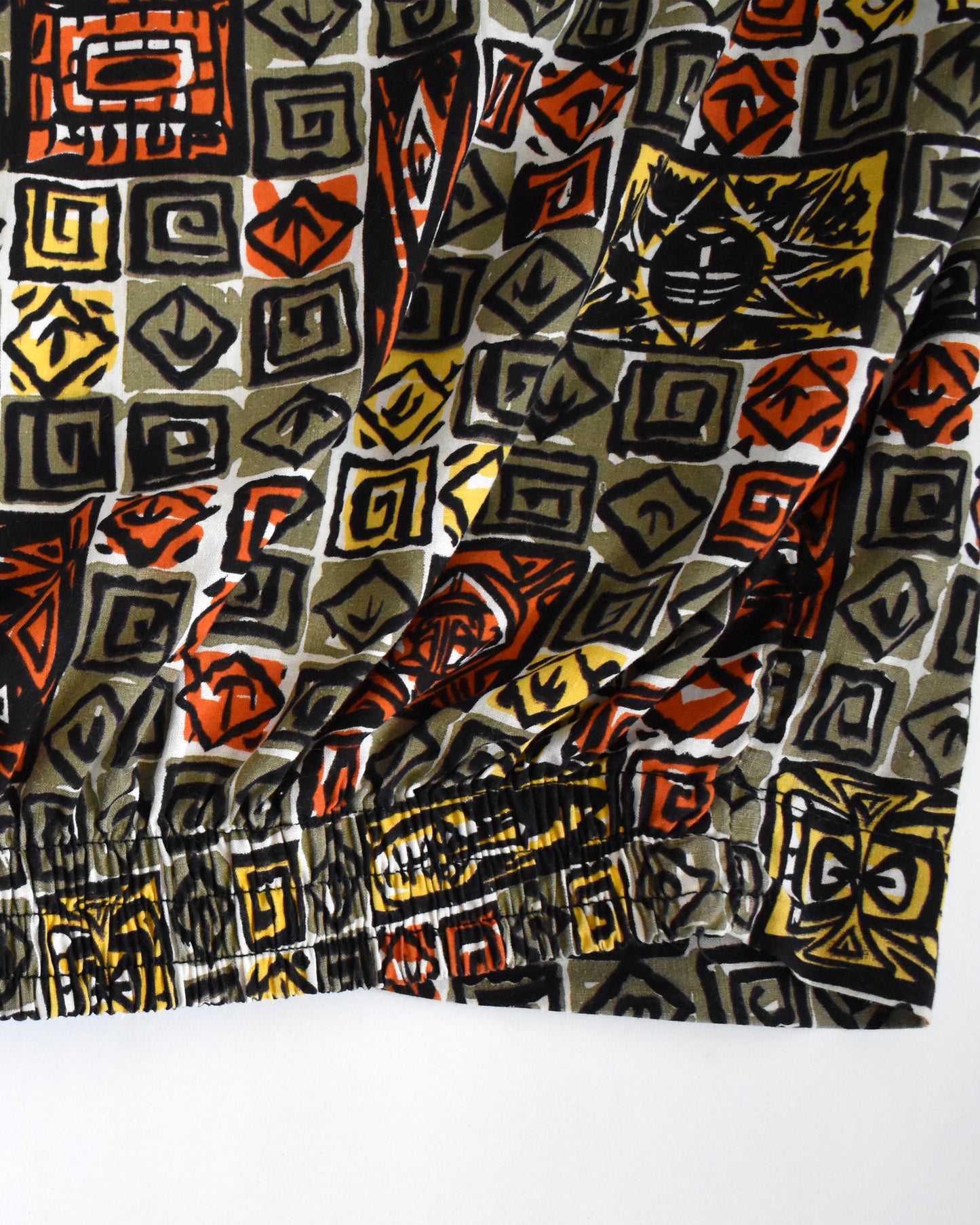 close up of the elastic hem on a vintage 1960s short-sleeve cabana shirt with geometric pattern on a white background
