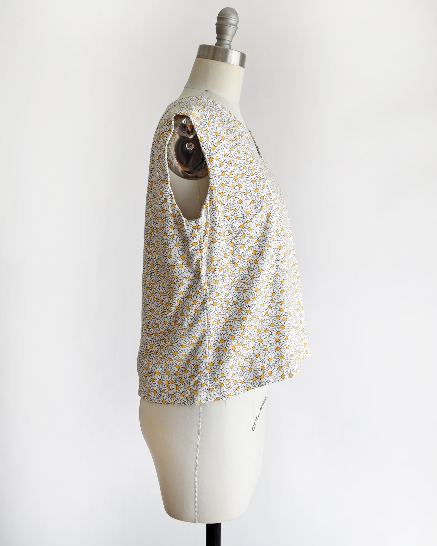 side view of a vintage floral sleeveless top on a mannequin with 'Collapsible Shoulder' label against a white background