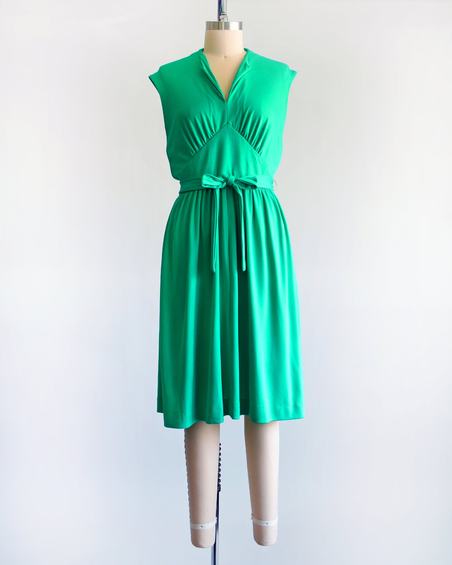 a vintage emerald green dress that has tie wrap around the waist. the dress is on a dress form