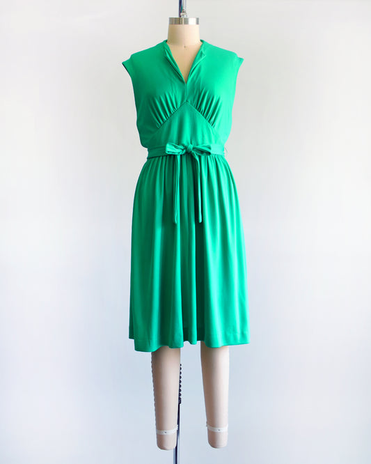a vintage emerald green dress that has tie wrap around the waist. the dress is on a dress form