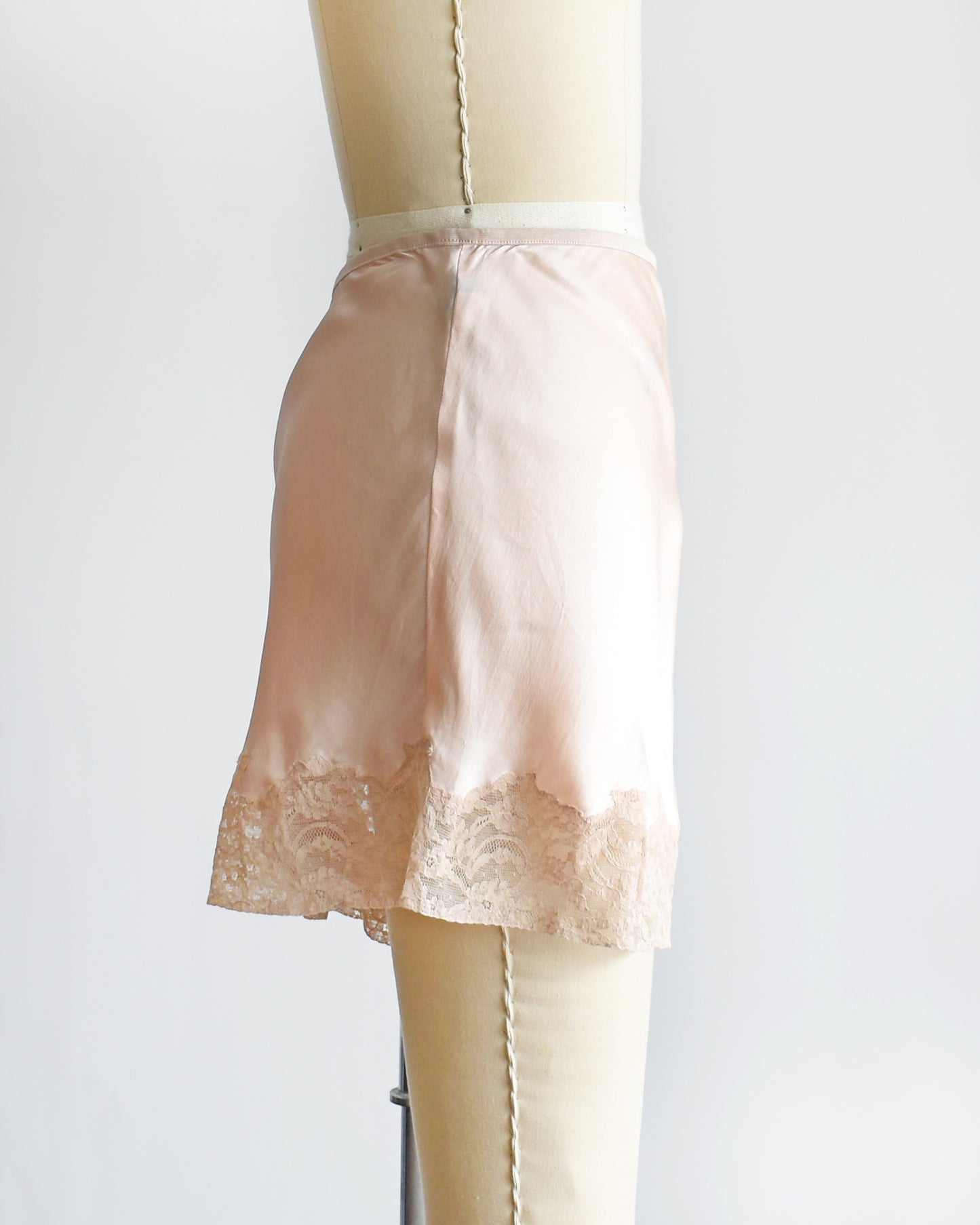 side view of vintage 1940s light peach silk shorts with lace trim on a dress form