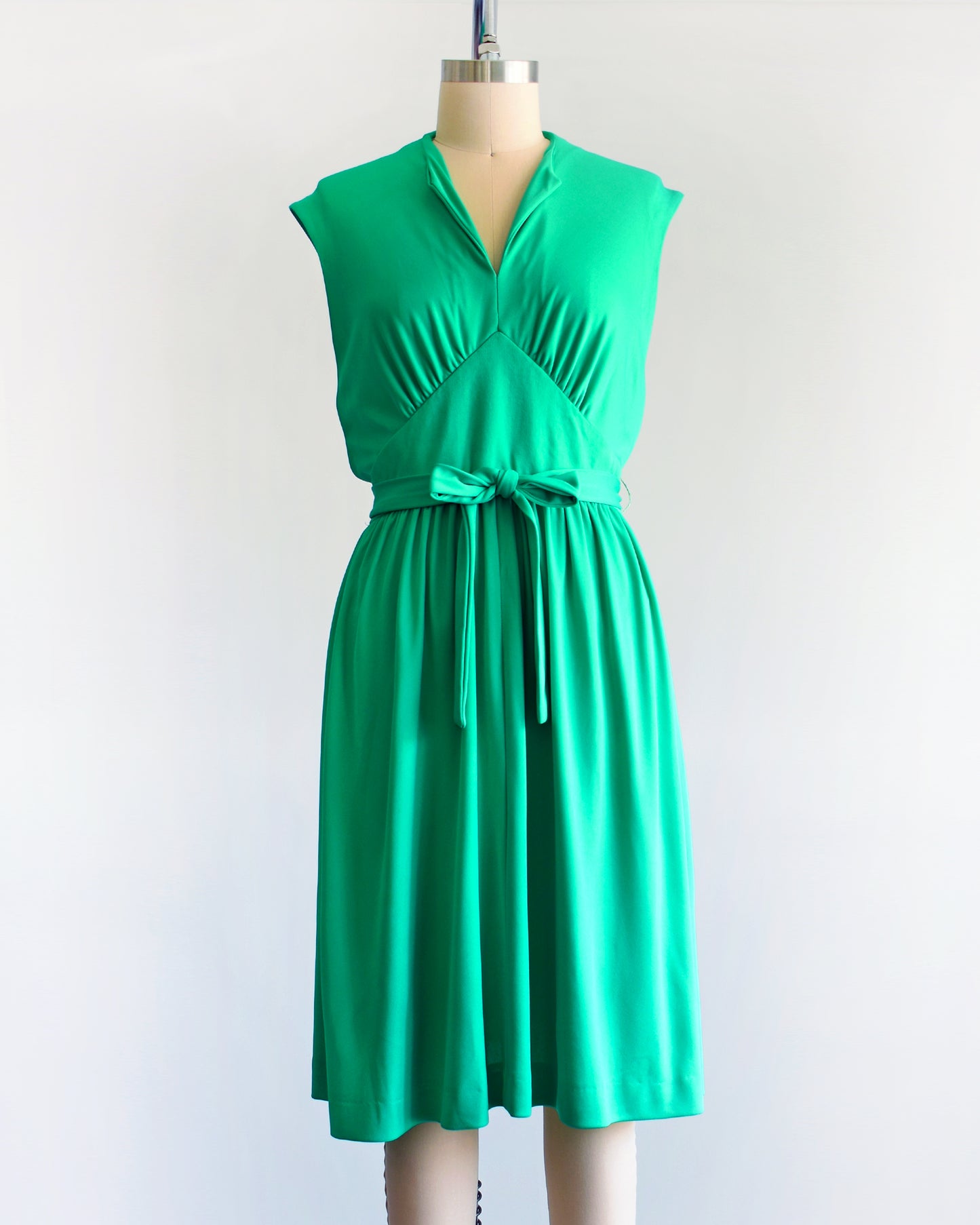 a vintage emerald green dress that has tie wrap around the waist. the dress is on a dress form