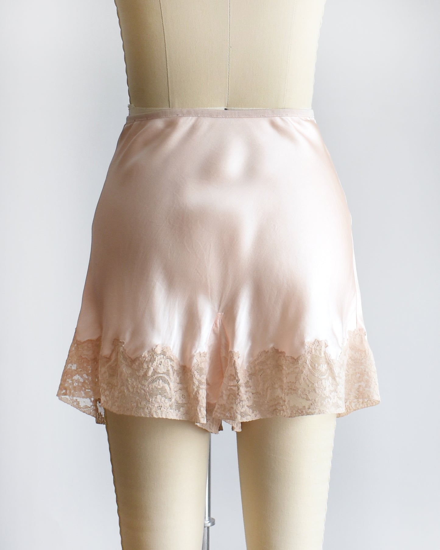 back view of vintage 1940s light peach silk shorts with lace trim on a dress form