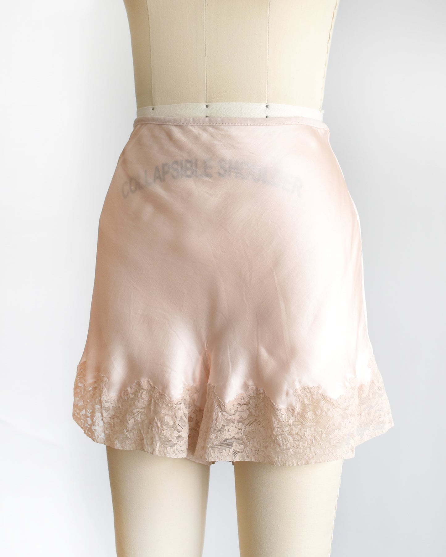 side front view of a vintage 1940s light peach silk shorts with lace trim on a dress form