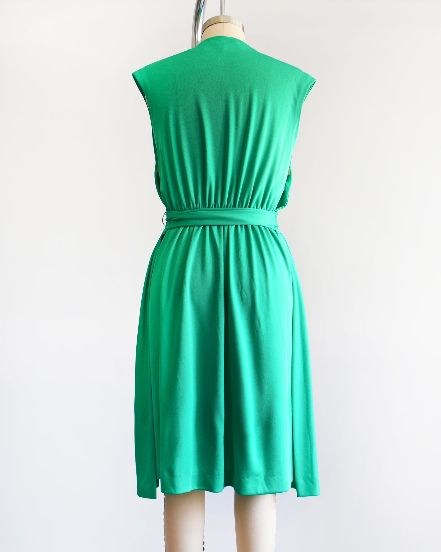 back view of a vintage emerald green dress that has tie wrap around the waist. the dress is on a dress form