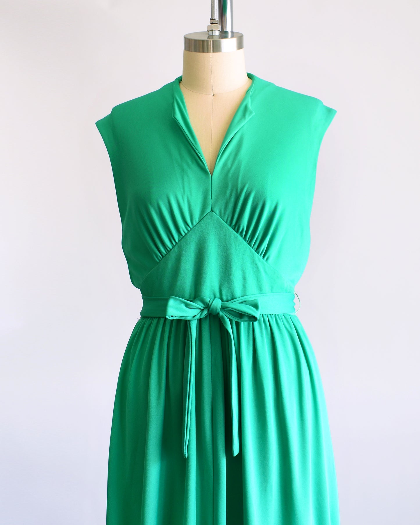 side front view of a vintage emerald green dress that has tie wrap around the waist. the dress is on a dress form