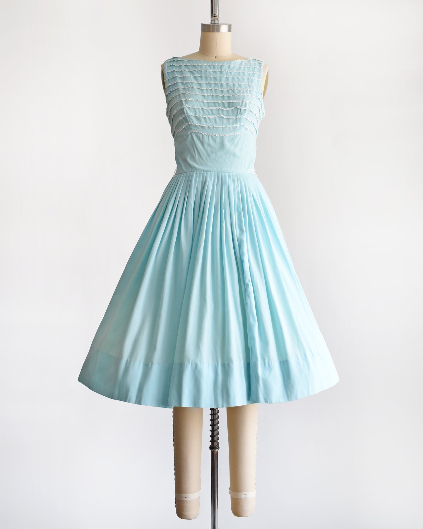 A vintage 1950s blue fit and flare dress that has white lace trim on the bodice on a dress form