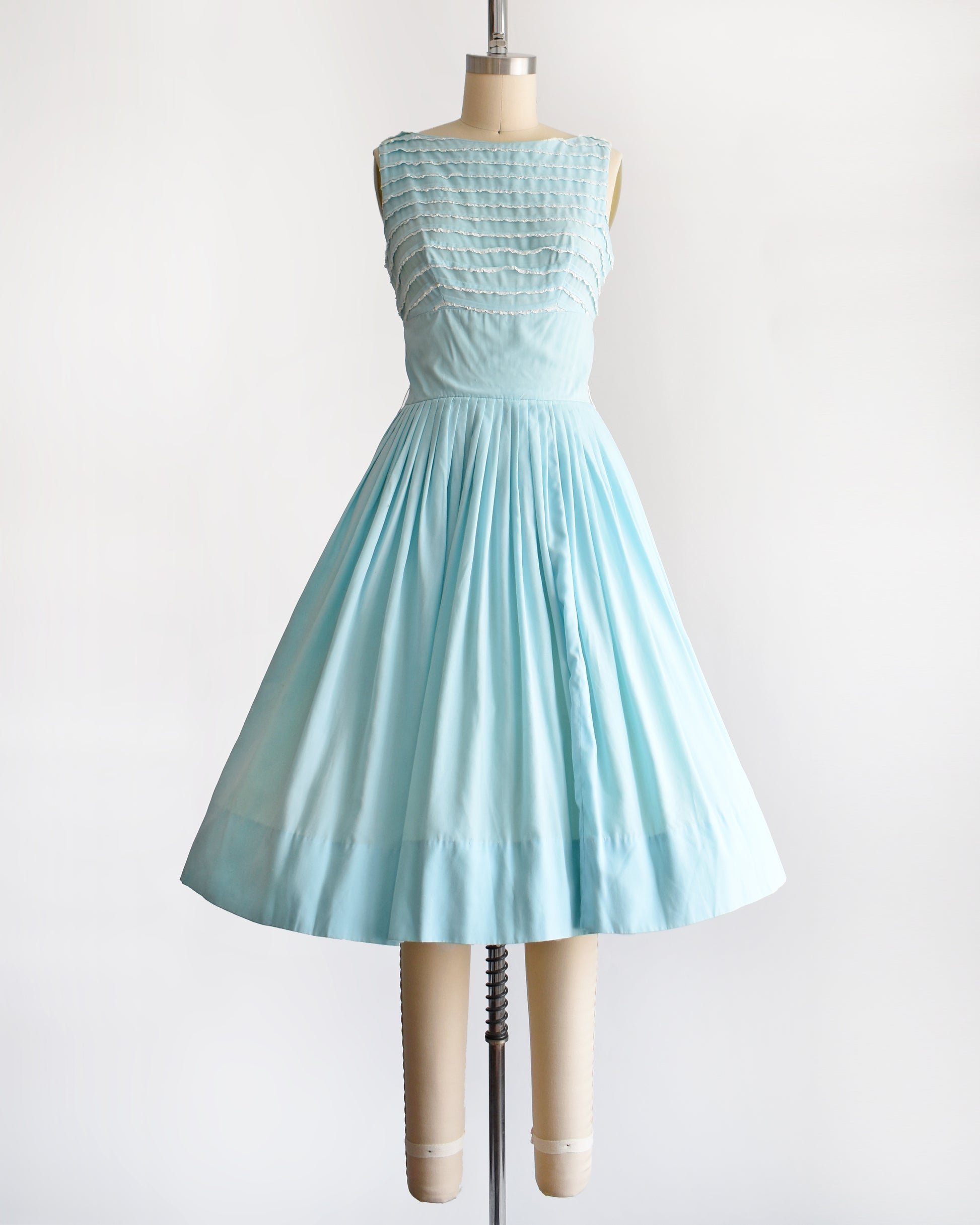 A vintage 1950s blue fit and flare dress that has white lace trim on the bodice on a dress form
