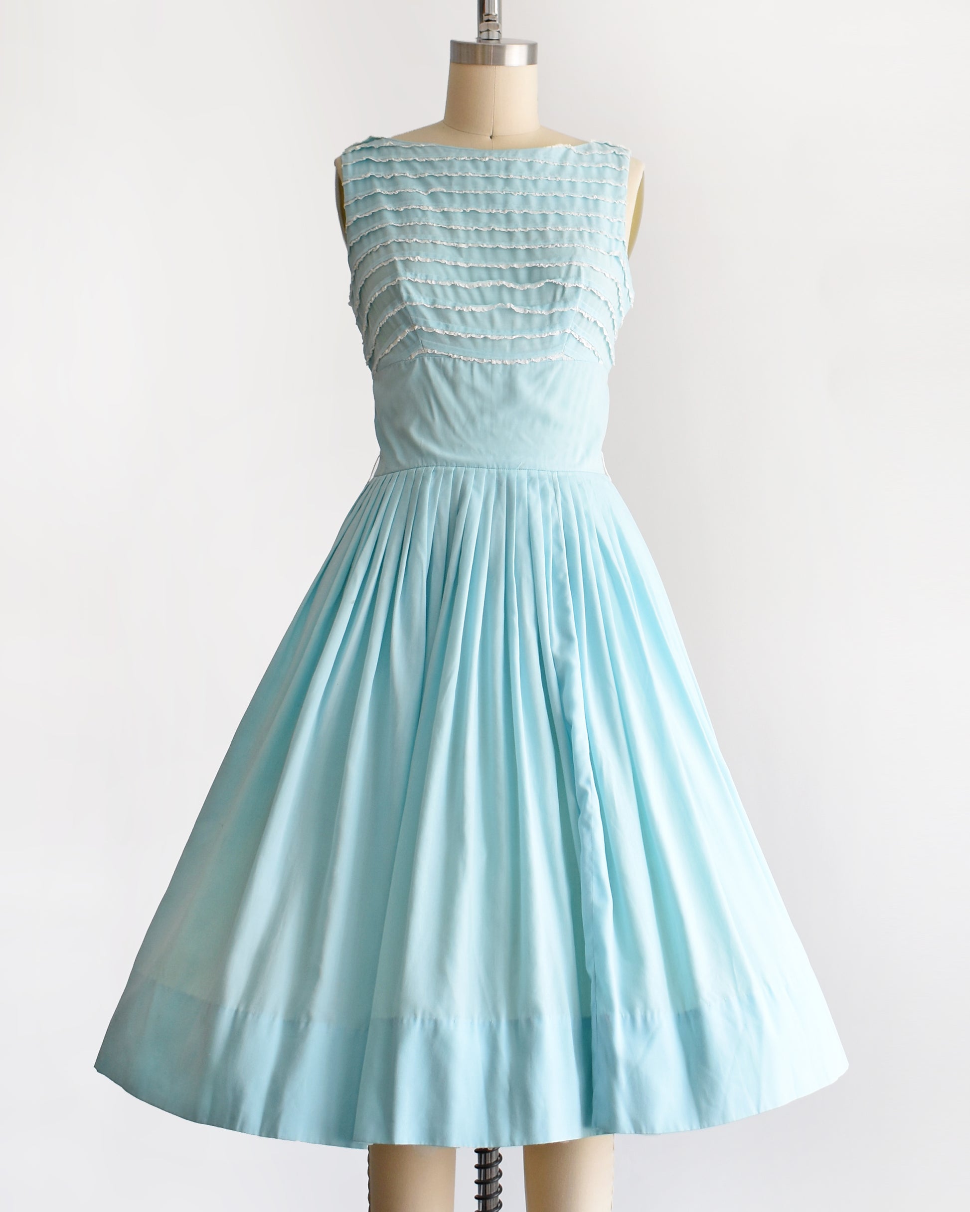 A vintage 1950s blue fit and flare dress that has white lace trim on the bodice on a dress form
