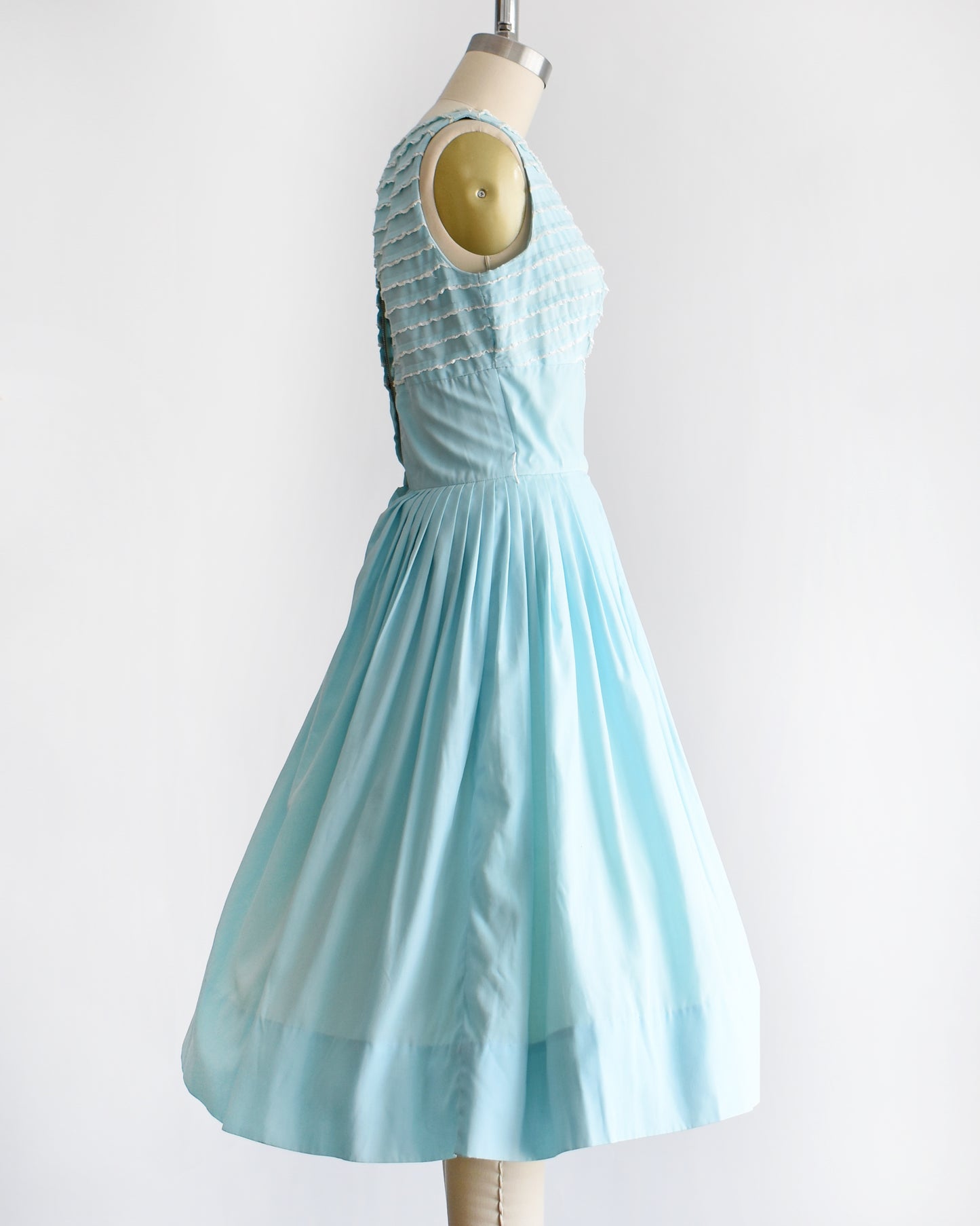 side view of a vintage 1950s blue fit and flare dress that has white lace trim on the bodice on a dress form