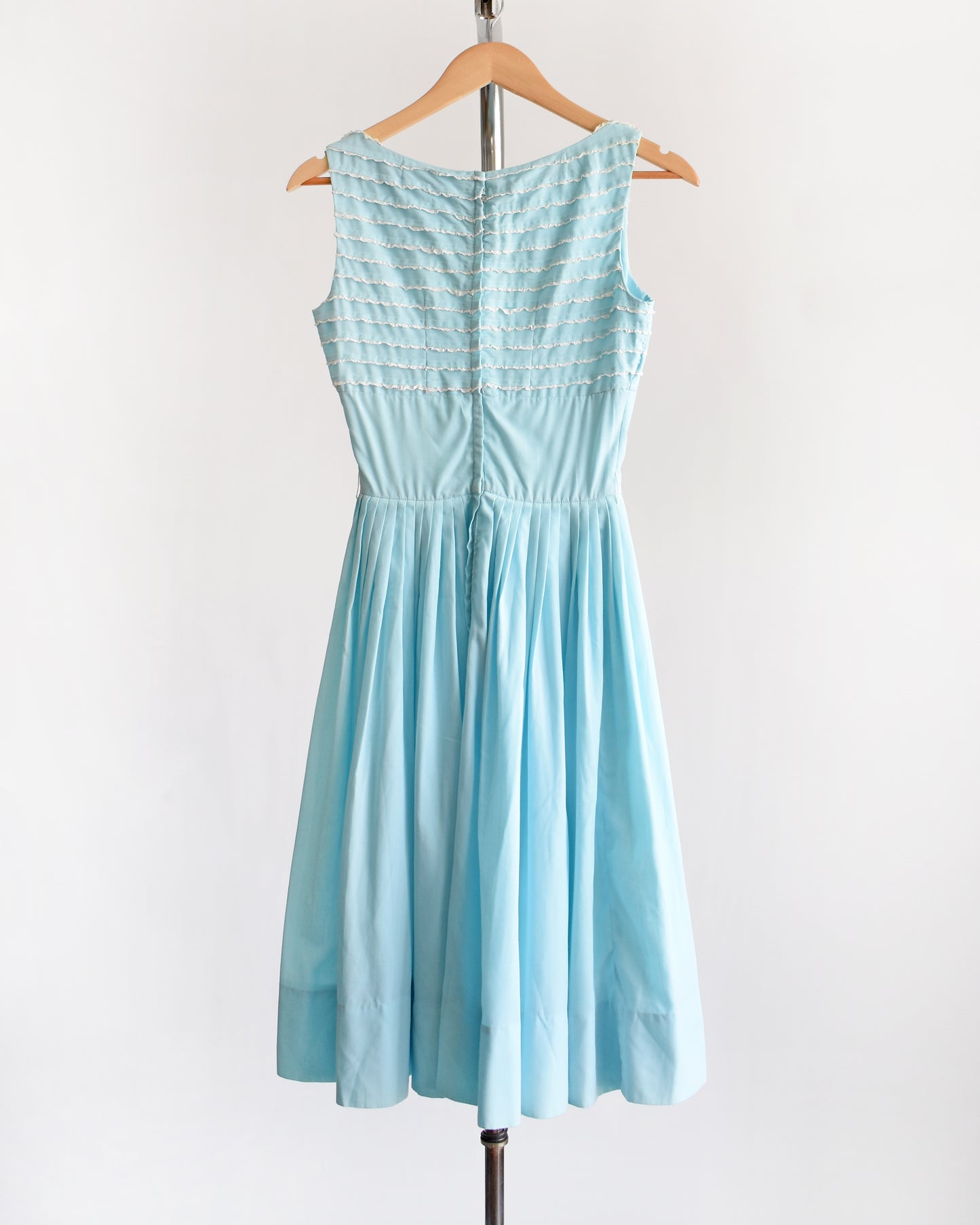 a vintage 1950s blue fit and flare dress that has white lace trim on the bodice on a hanger