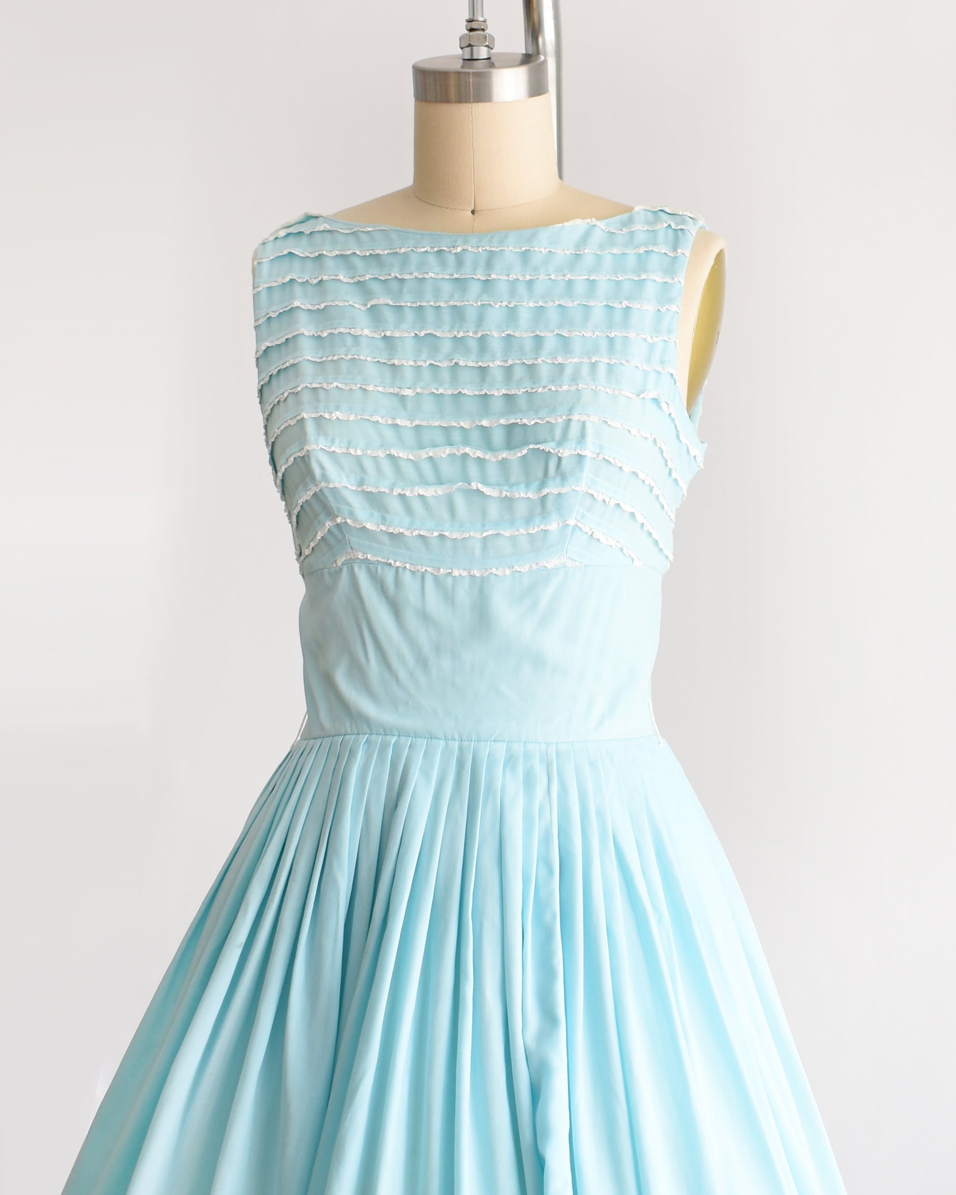 side front view of a vintage 1950s blue fit and flare dress that has white lace trim on the bodice on a dress form