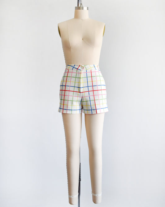 A pair of vintage 1970s white shorts with rainbow plaid stripes on a dress form.