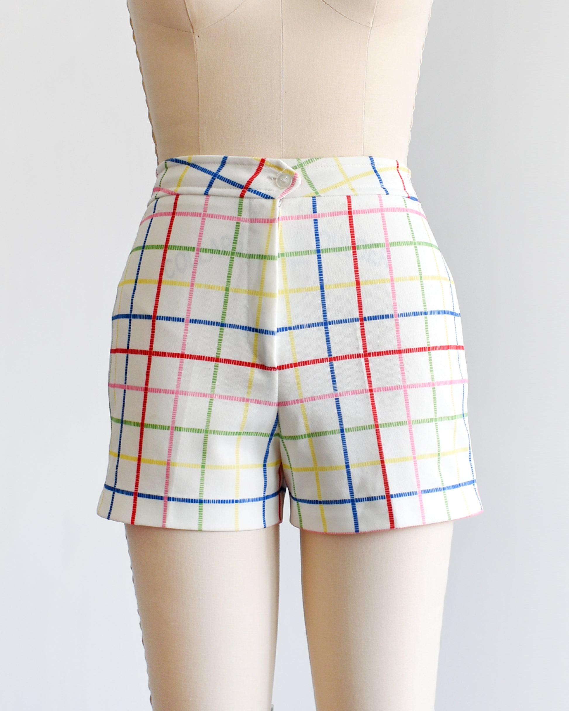 A pair of vintage 1970s white shorts with rainbow plaid stripes on a dress form.