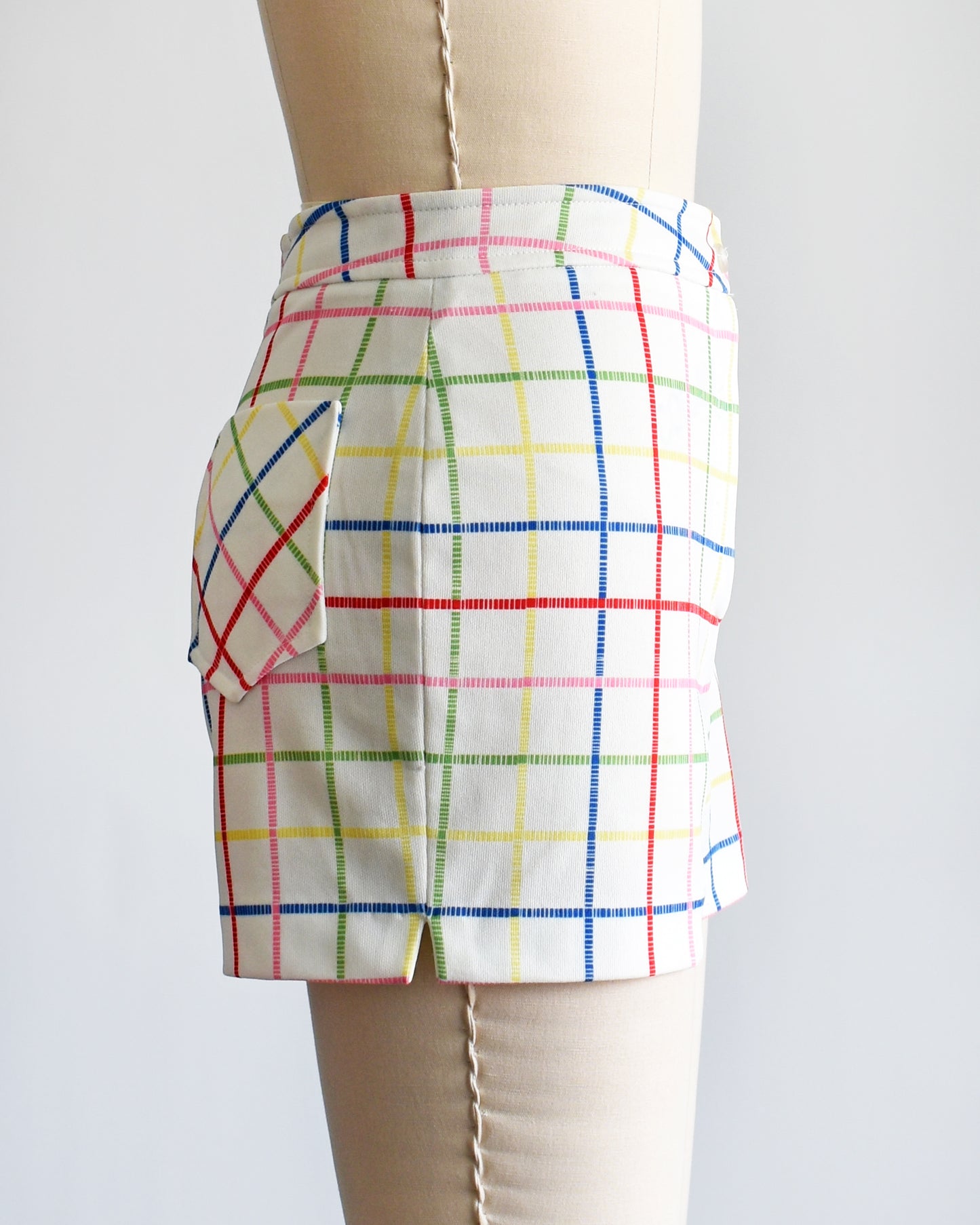 side view of a pair of vintage 1970s white shorts with rainbow plaid stripes on a dress form.