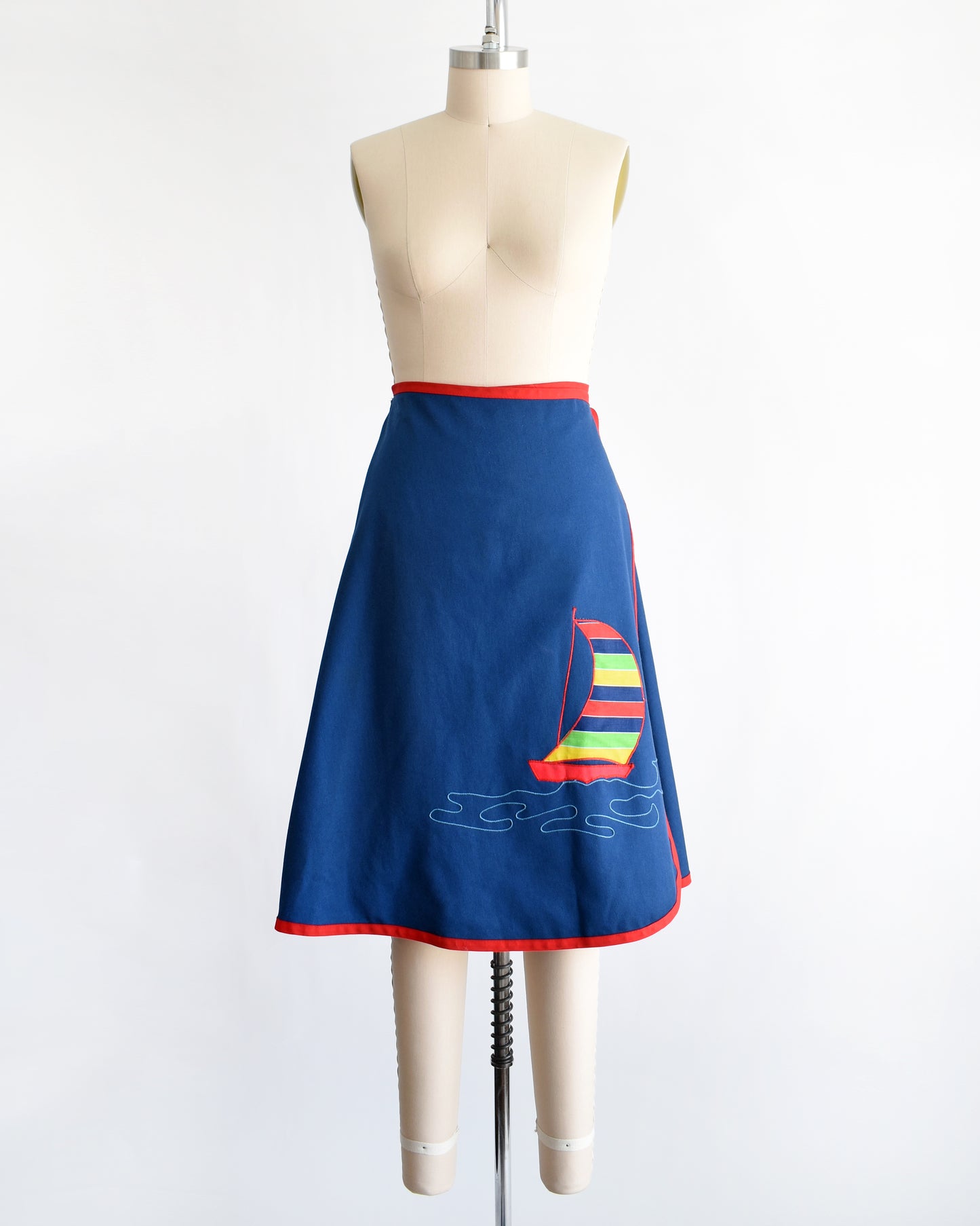 a vintage blue wrap skirt with a colorful sailboat design on a mannequin against a white background