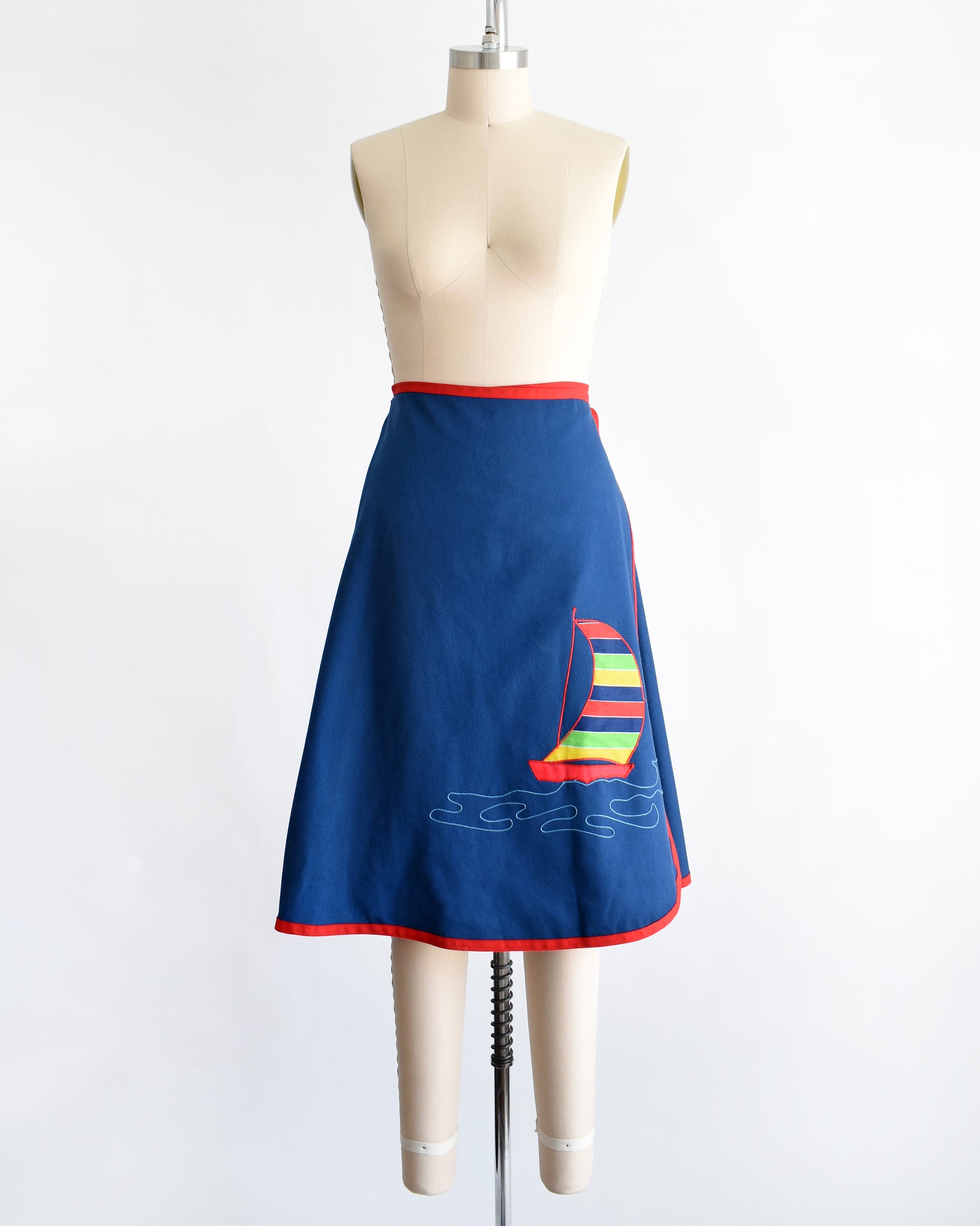 a vintage blue wrap skirt with a colorful sailboat design on a mannequin against a white background