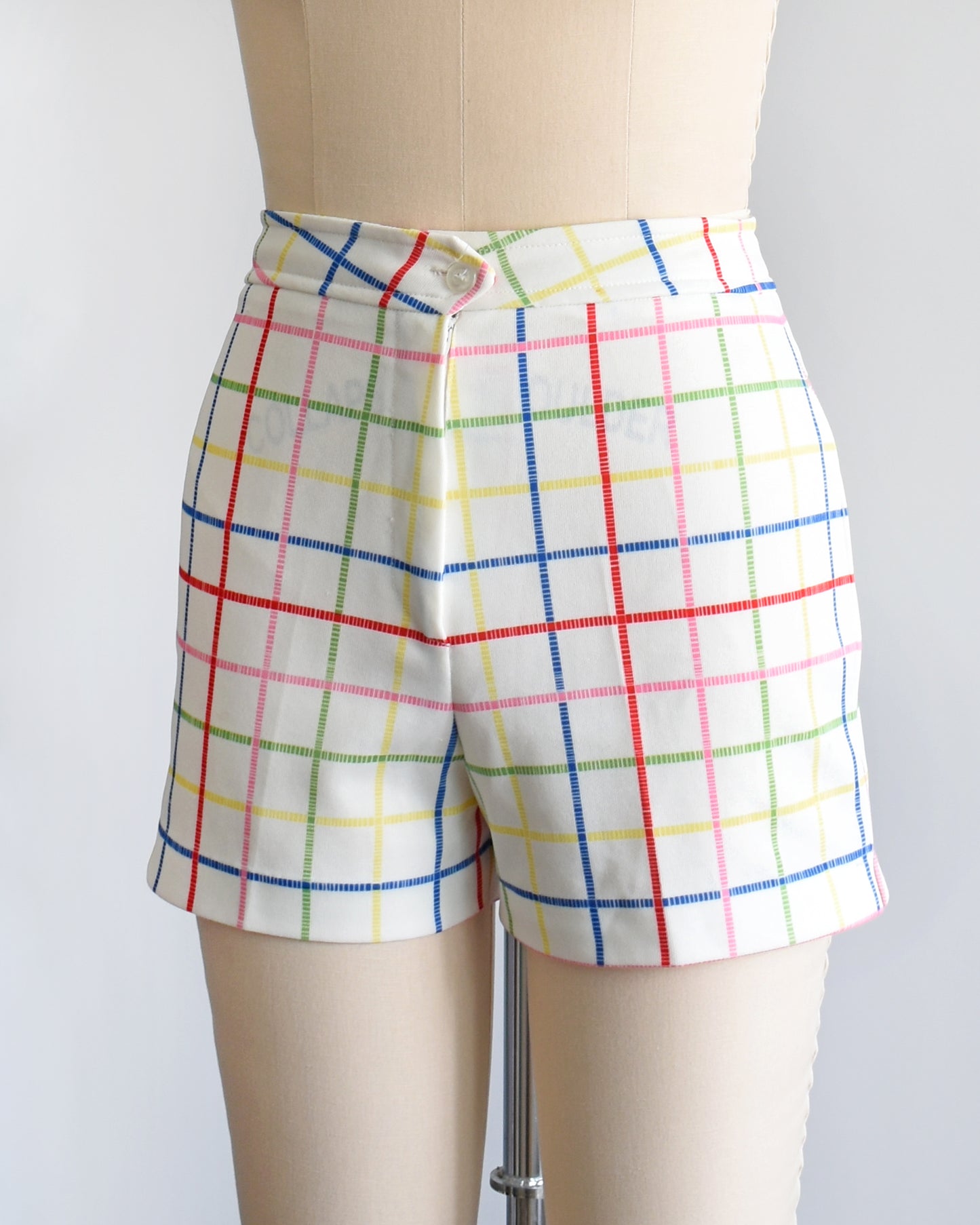 side front view of a pair of vintage 1970s white shorts with rainbow plaid stripes on a dress form.