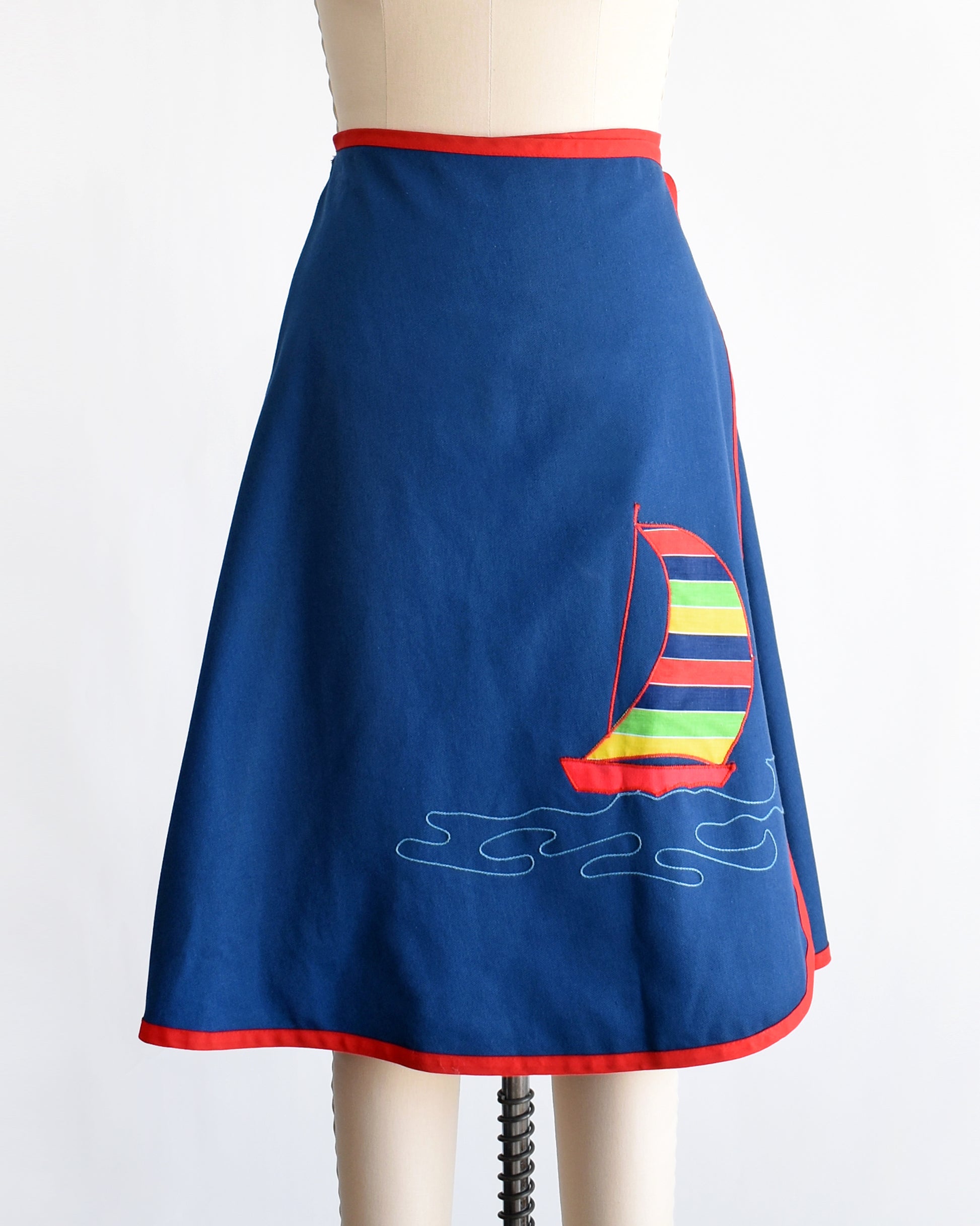 a vintage blue wrap skirt with a colorful sailboat design on a mannequin against a white background