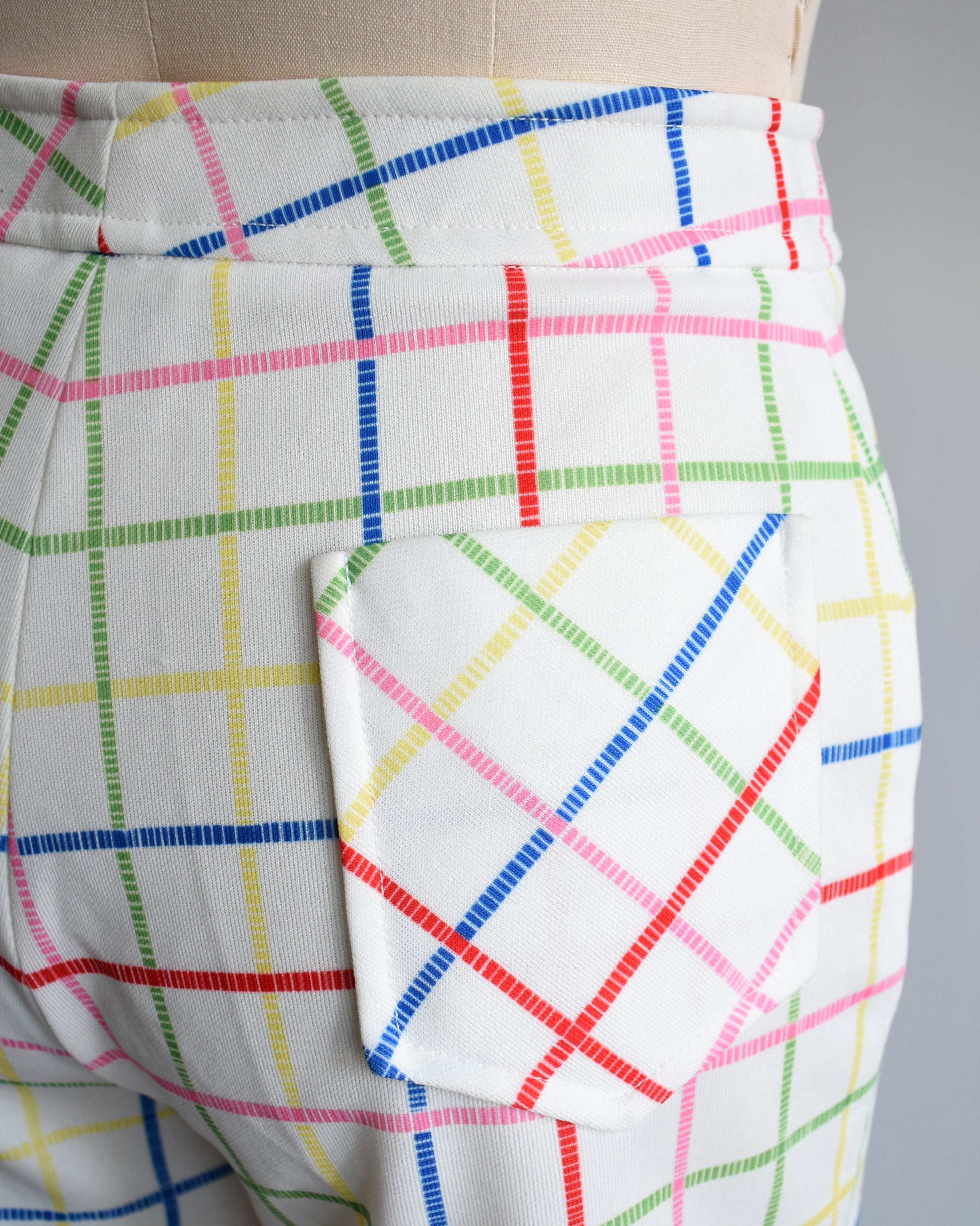 close up of the back pocket on a a pair of vintage 1970s white shorts with rainbow plaid stripes on a dress form.